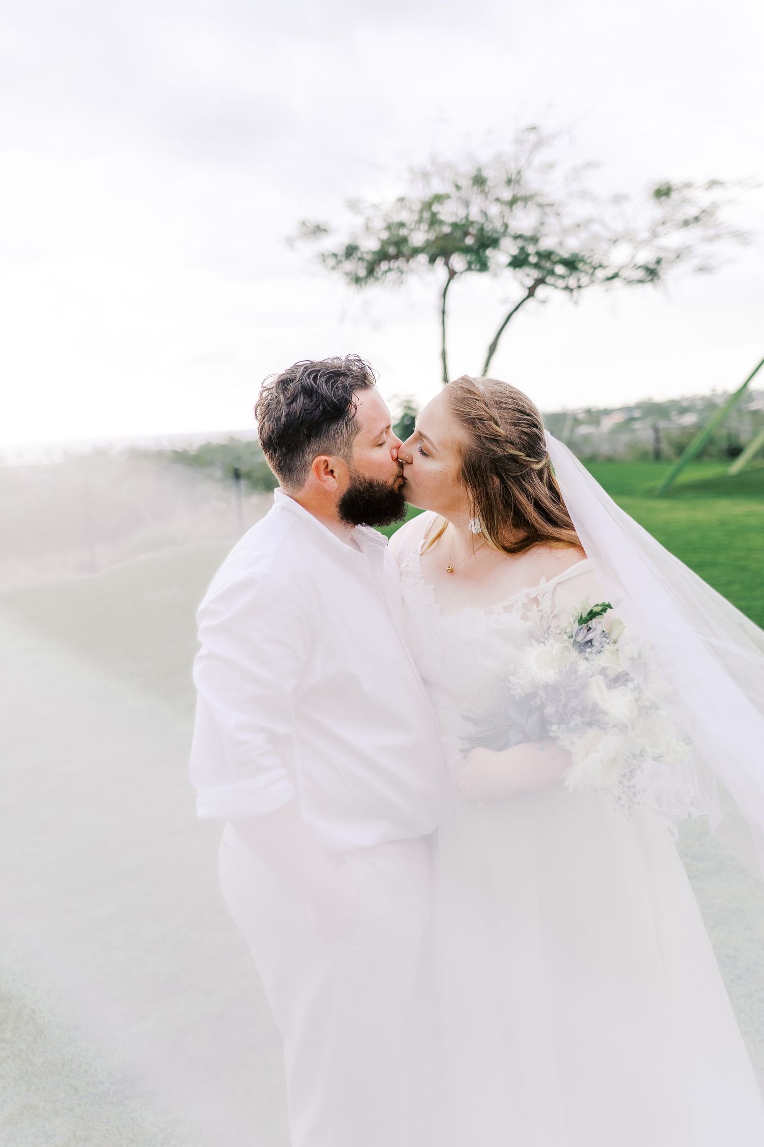 Romantic wedding portrait with flowing veil in outdoor garden setting.