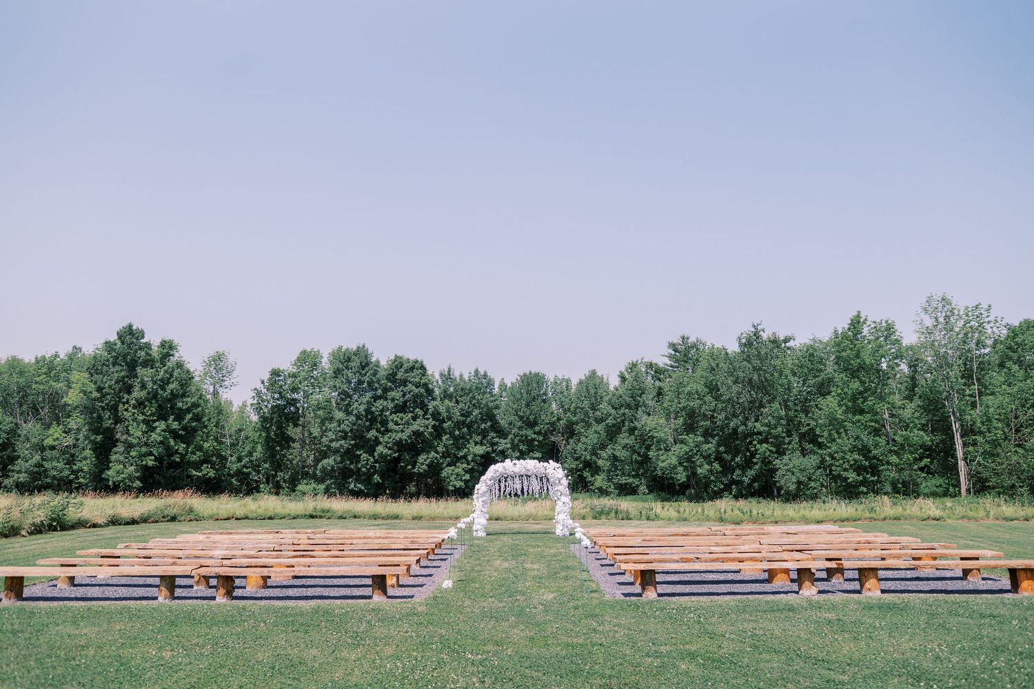 Panoramic view of long freight train cars lined up on parallel tracks with green trees in the background against blue sky.