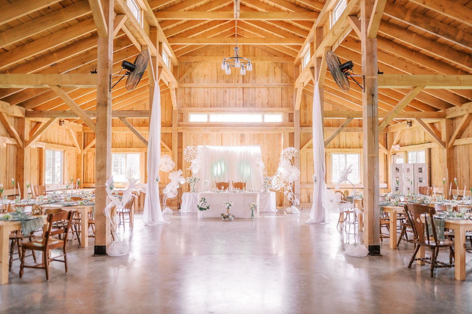 Panoramic interior view of a rustic wooden barn event venue with exposed beams, chandeliers and natural lighting.