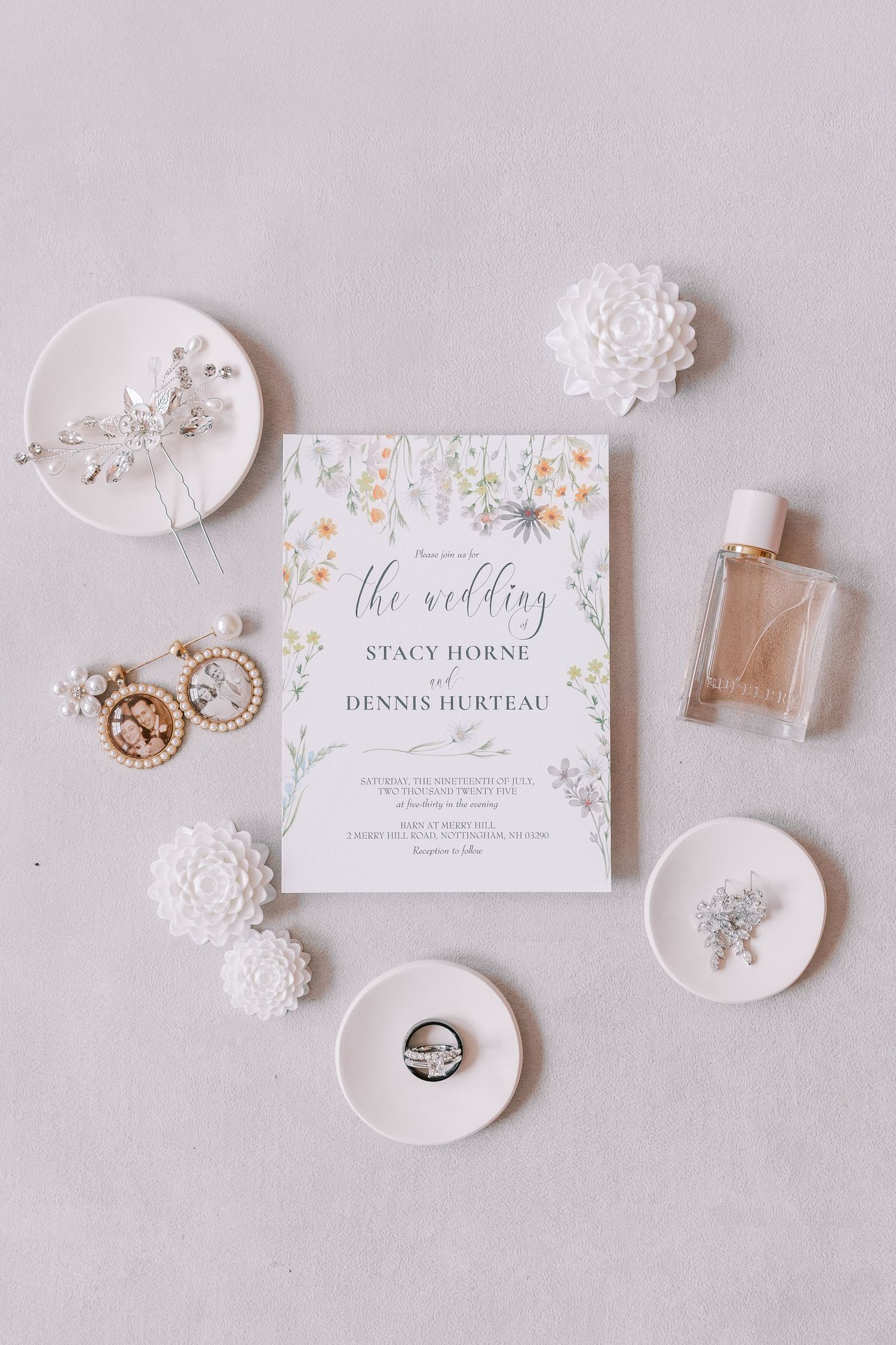 Elegant wedding invitation flatlay with floral design and white accessories including rings and perfume bottle.