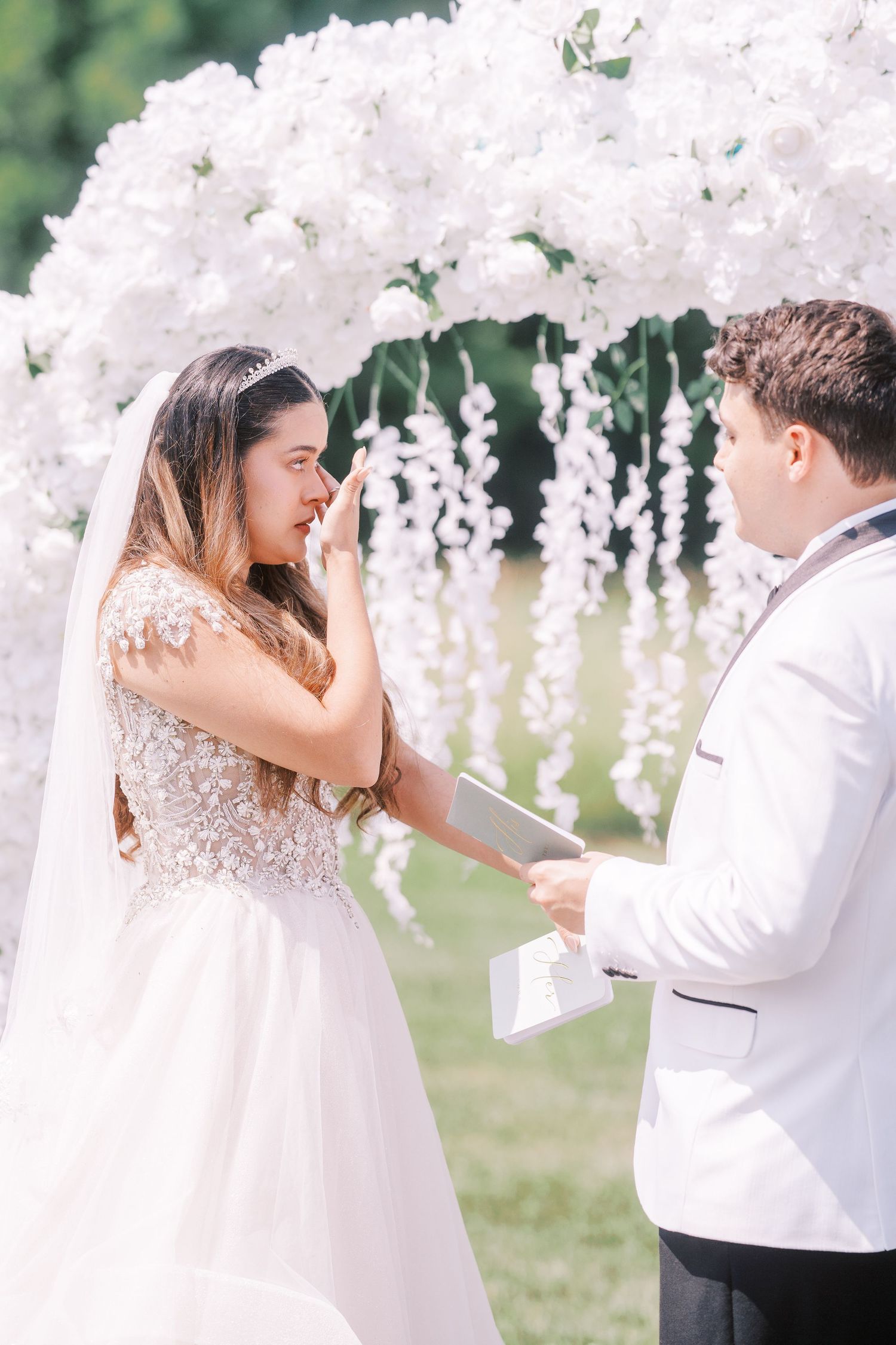 Bride and groom share a joyful first look moment in an outdoor garden setting surrounded by delicate white flowers.