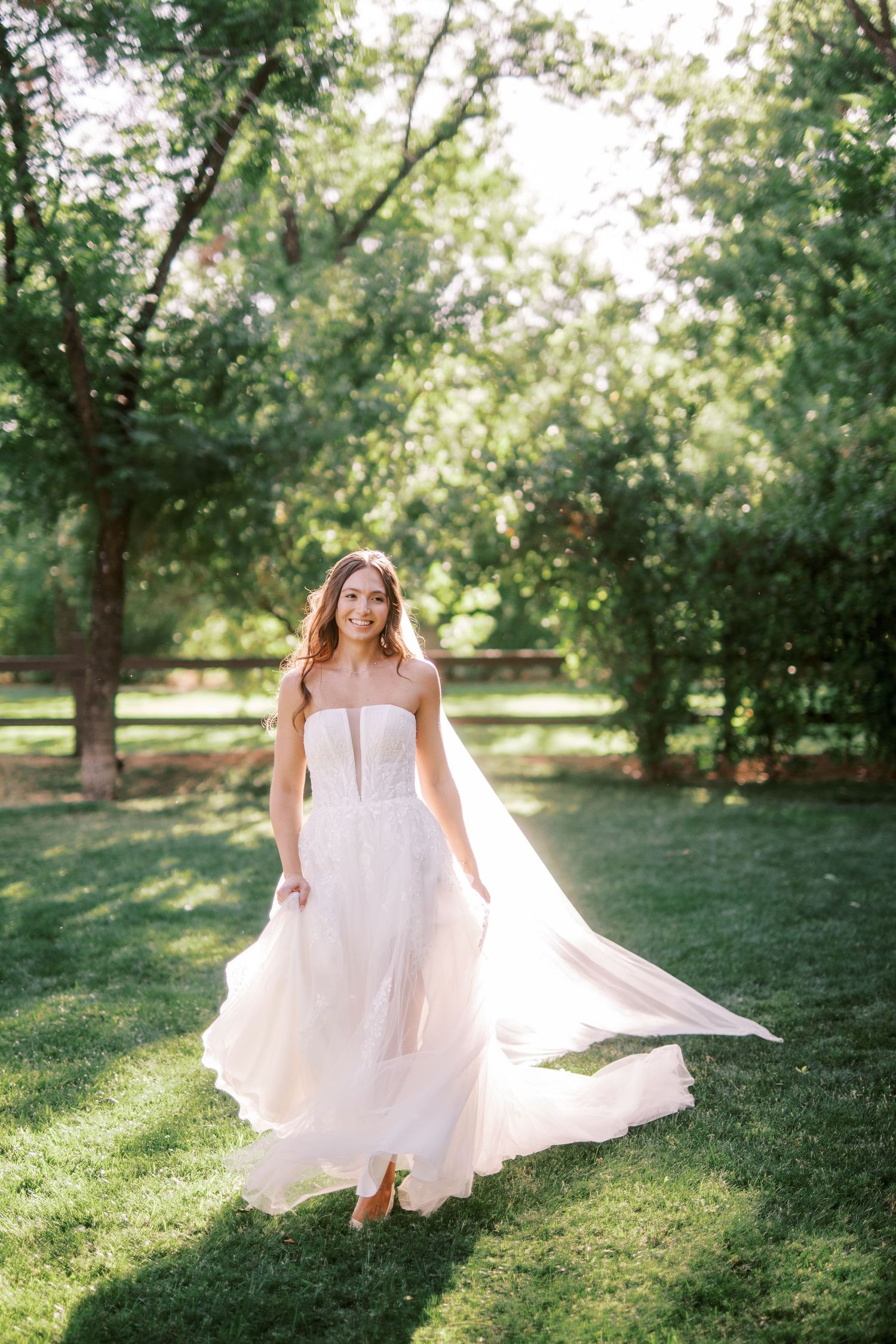 A joyful bride in a flowing white dress twirls gracefully in a sunlit garden setting creating a dreamy ethereal moment.