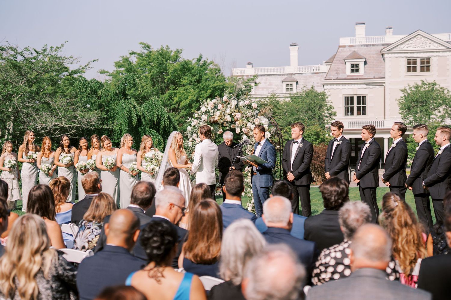 An outdoor wedding ceremony takes place on a rooftop venue with elegant decor and guests gathered beneath a sunny sky.