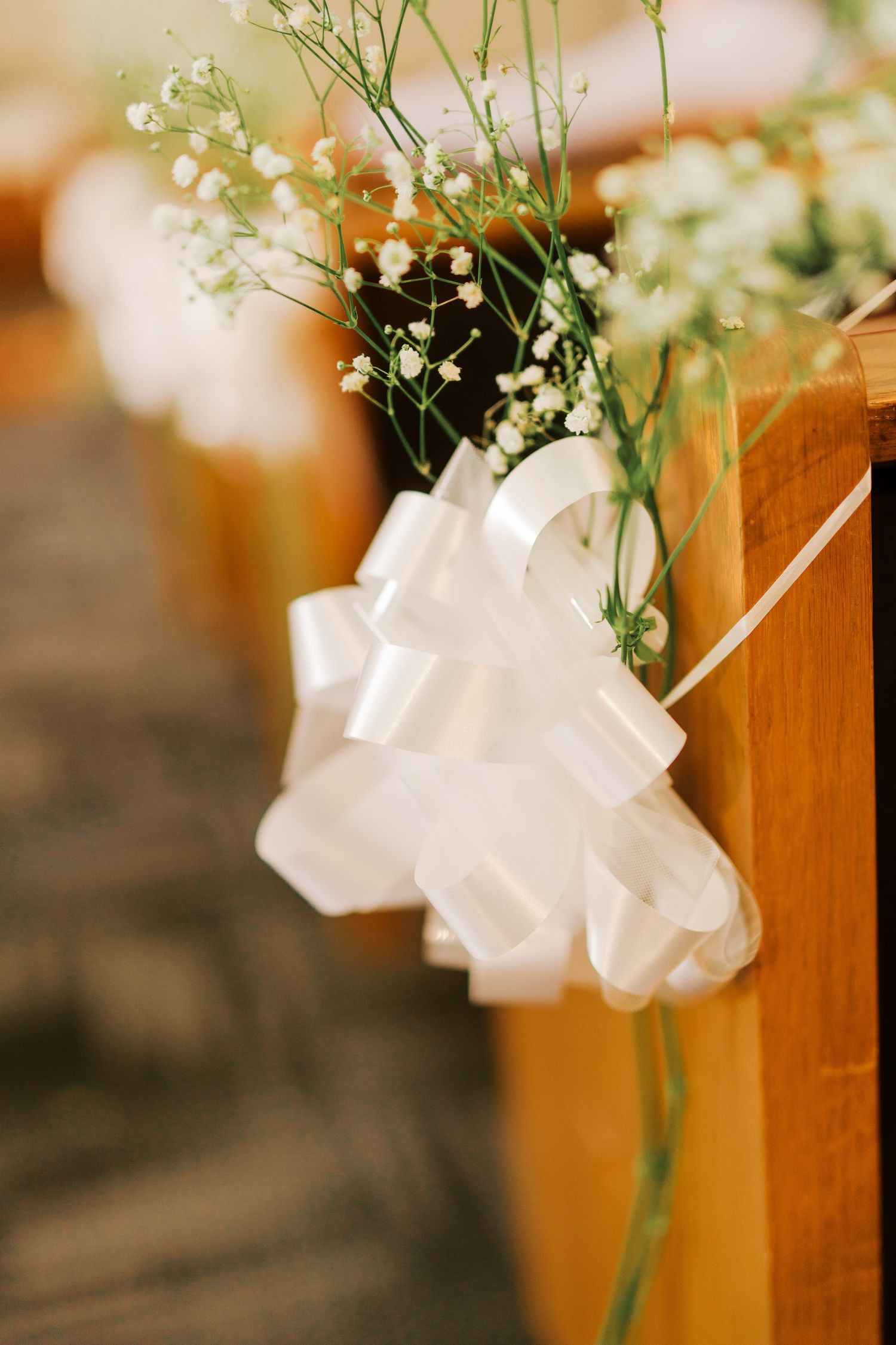 Delicate baby's breath flowers arranged in a white ribbon bow attached to a wooden church pew for wedding decor.