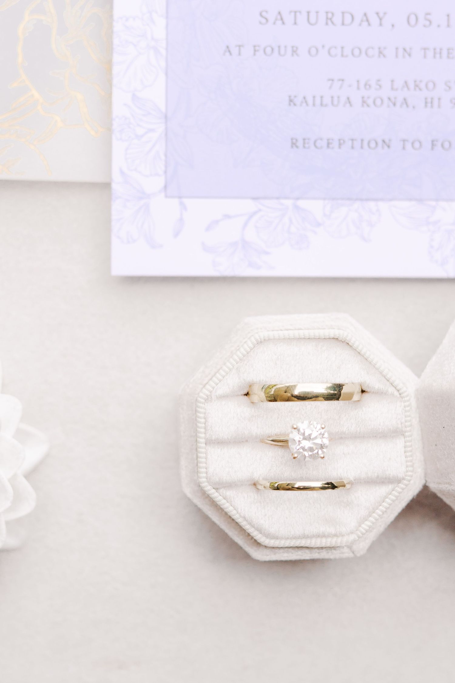 Wedding rings displayed in white octagonal ring box next to invitation.