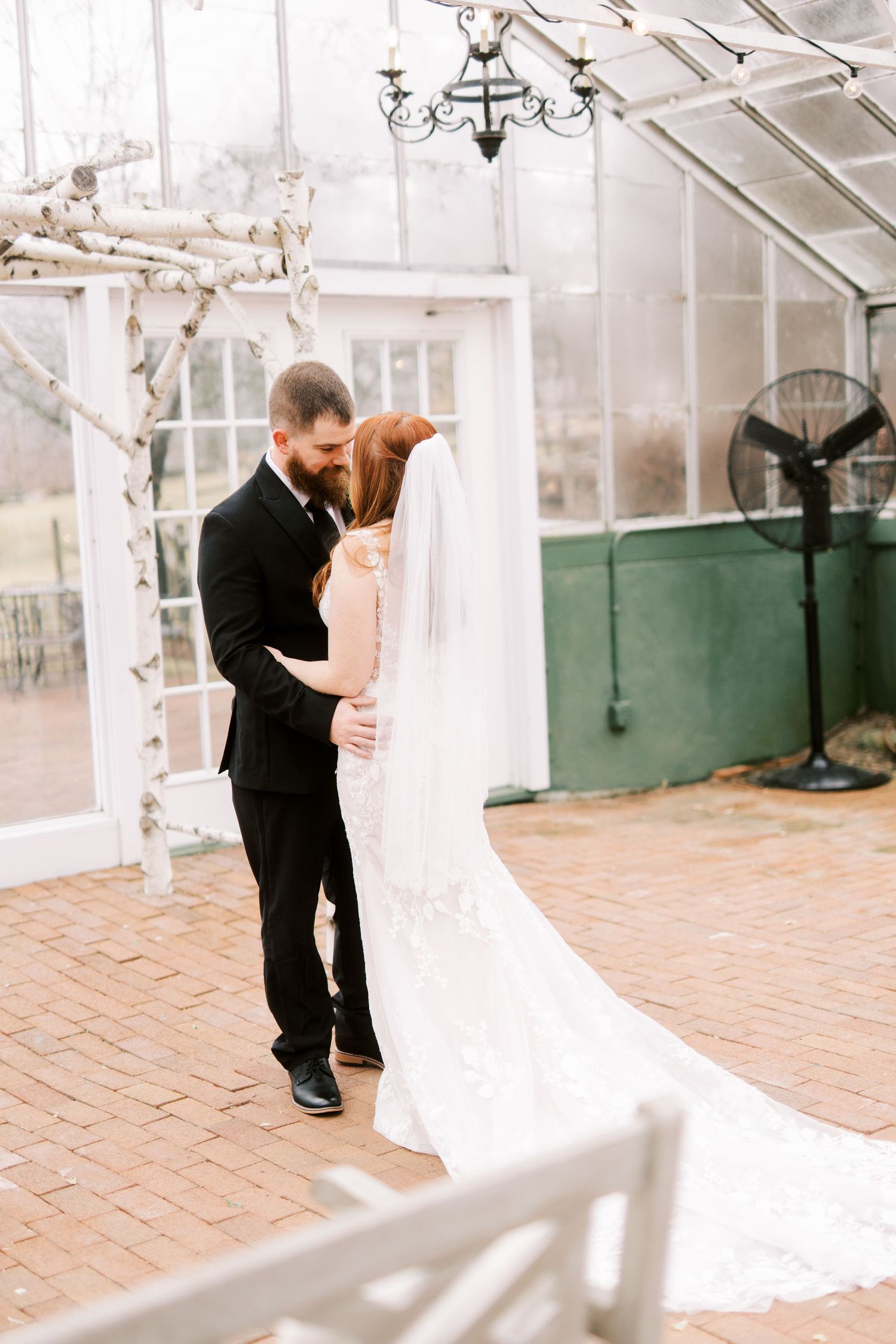 A romantic wedding moment captured in a greenhouse with brick flooring and a flowing white veil.