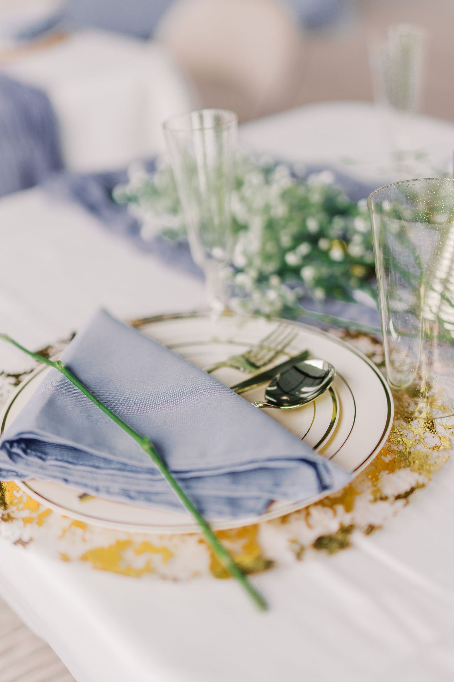 Close-up of wedding place setting with blue napkin, gold charger plate, and baby's breath flowers.