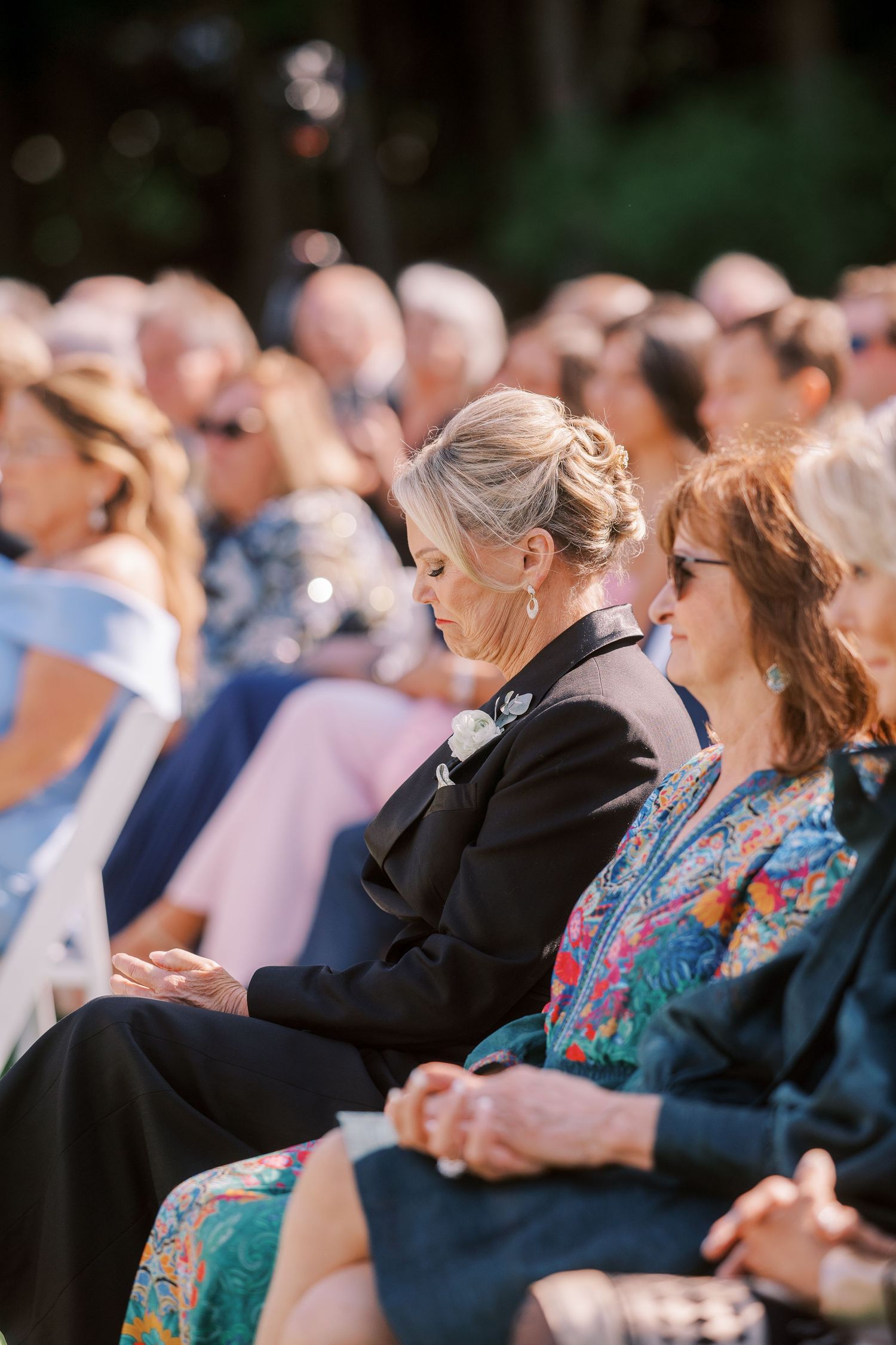 A crowd of senior citizens sitting together in rows at an outdoor event watching and clapping in unison.