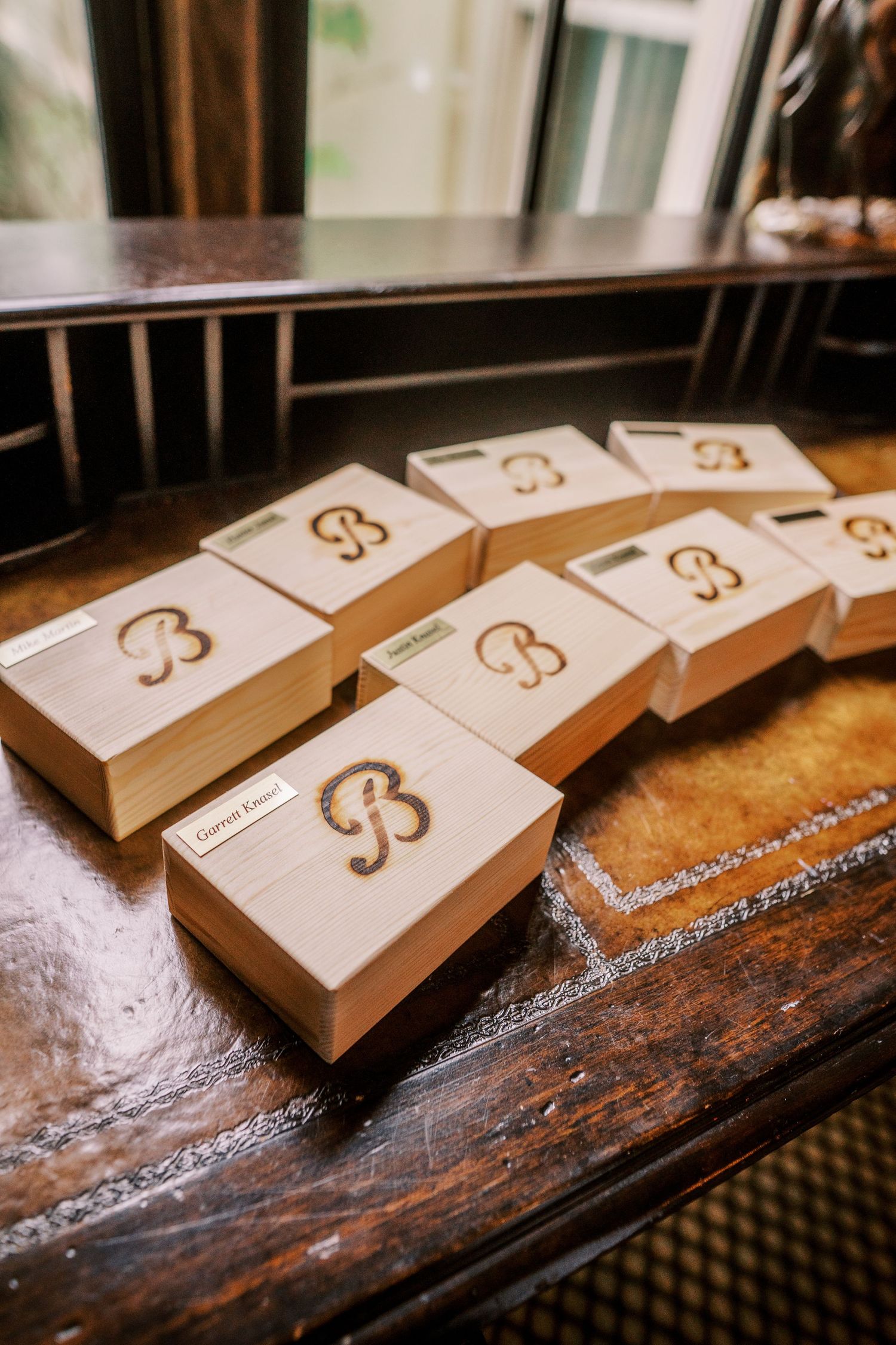 Multiple identical brown boxes with an elegant cursive monogram design arranged on a rustic wooden table surface.