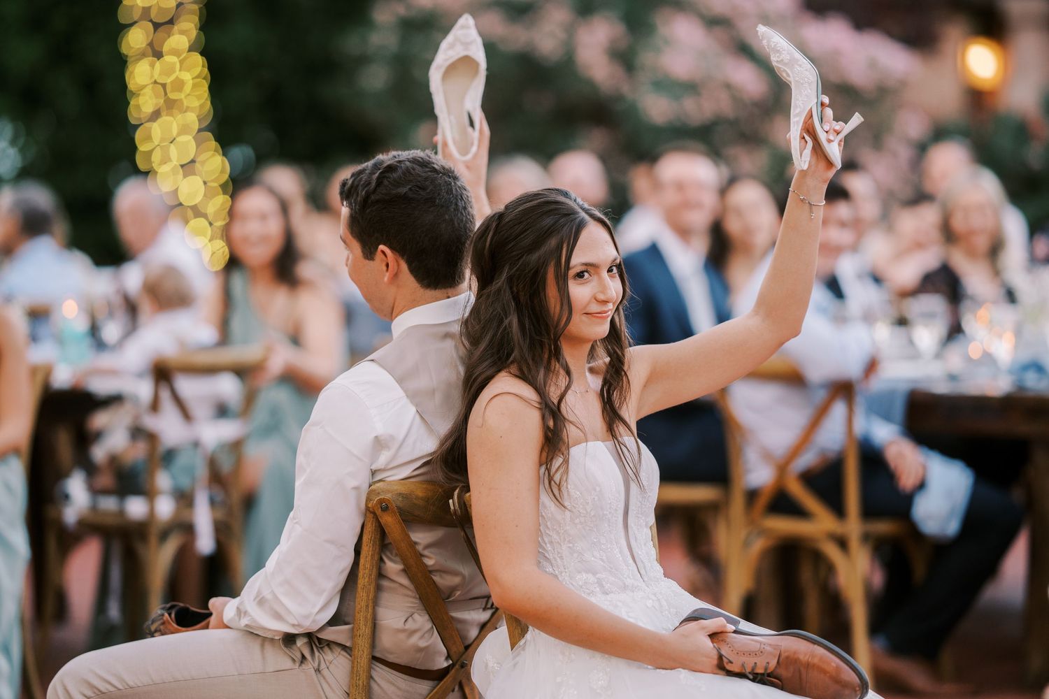 Wedding guests toast and celebrate during an outdoor evening reception under string lights and golden decor.
