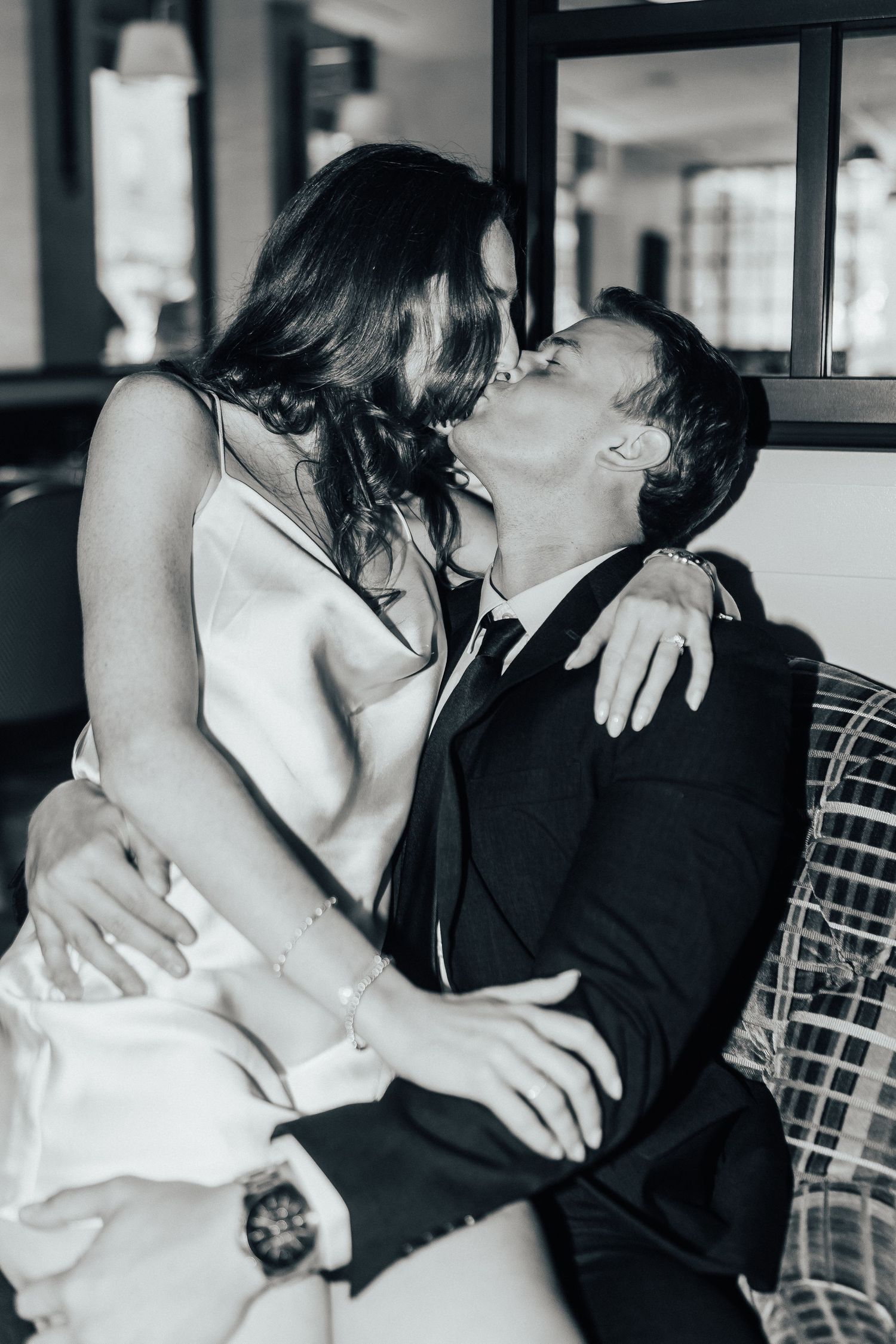 A romantic black and white photo of a couple sharing an intimate kiss while sitting together on a chair.