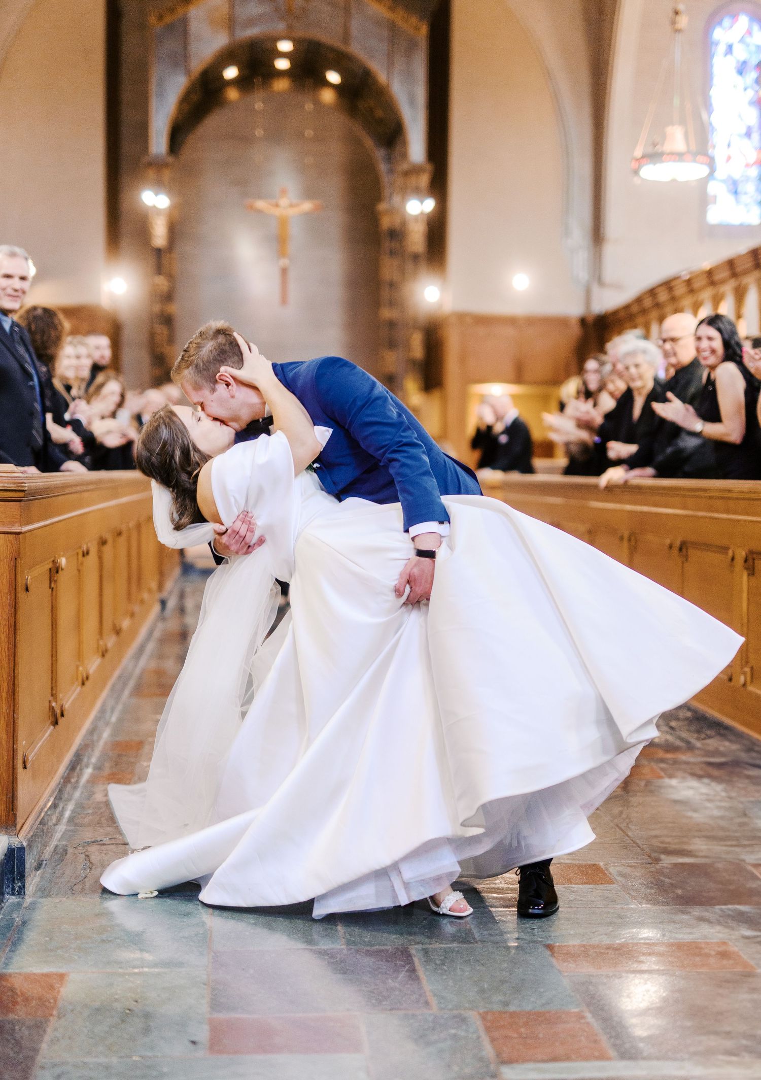 A couple shares a romantic dip kiss in a traditional church setting, with the bride in a flowing white gown.