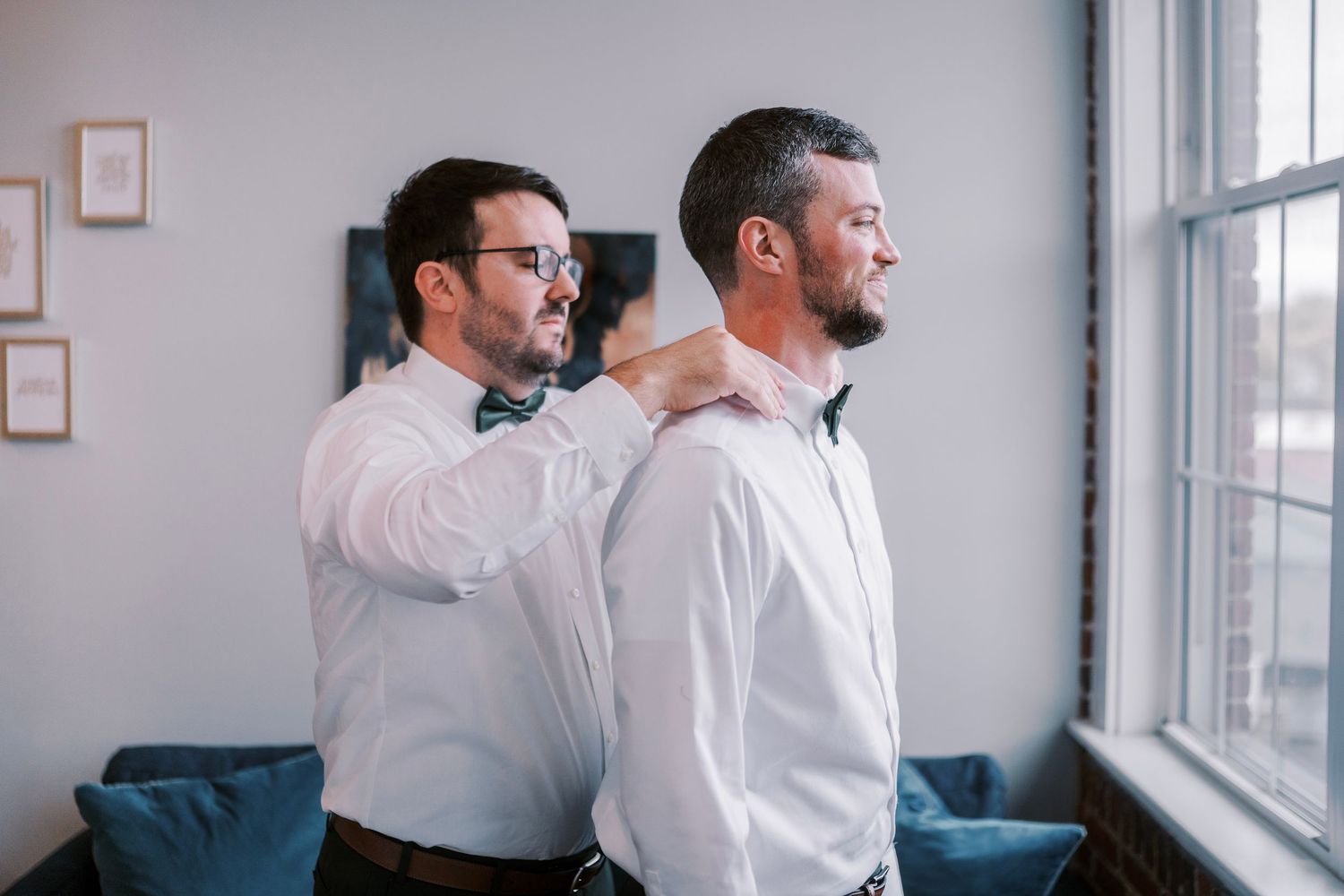 Two colleagues in white shirts stand by a window laughing together during a casual office moment.