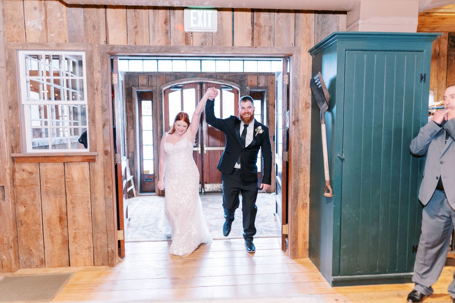 A newlywed couple walking through a rustic wooden doorway at their wedding venue.