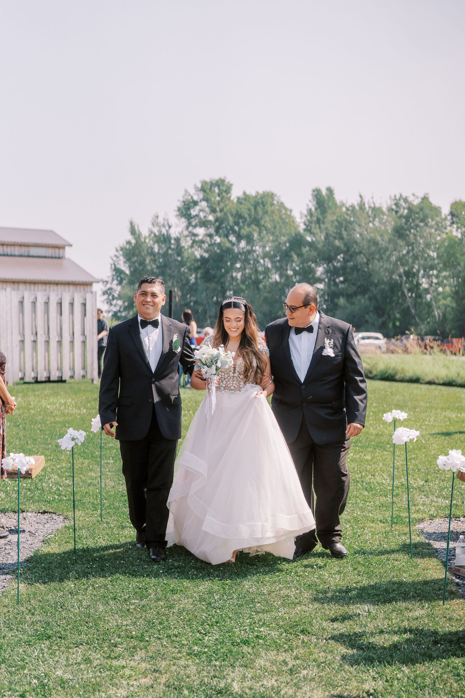 Wedding party members walk along a grassy path lined with white illuminated balloons during an outdoor celebration.