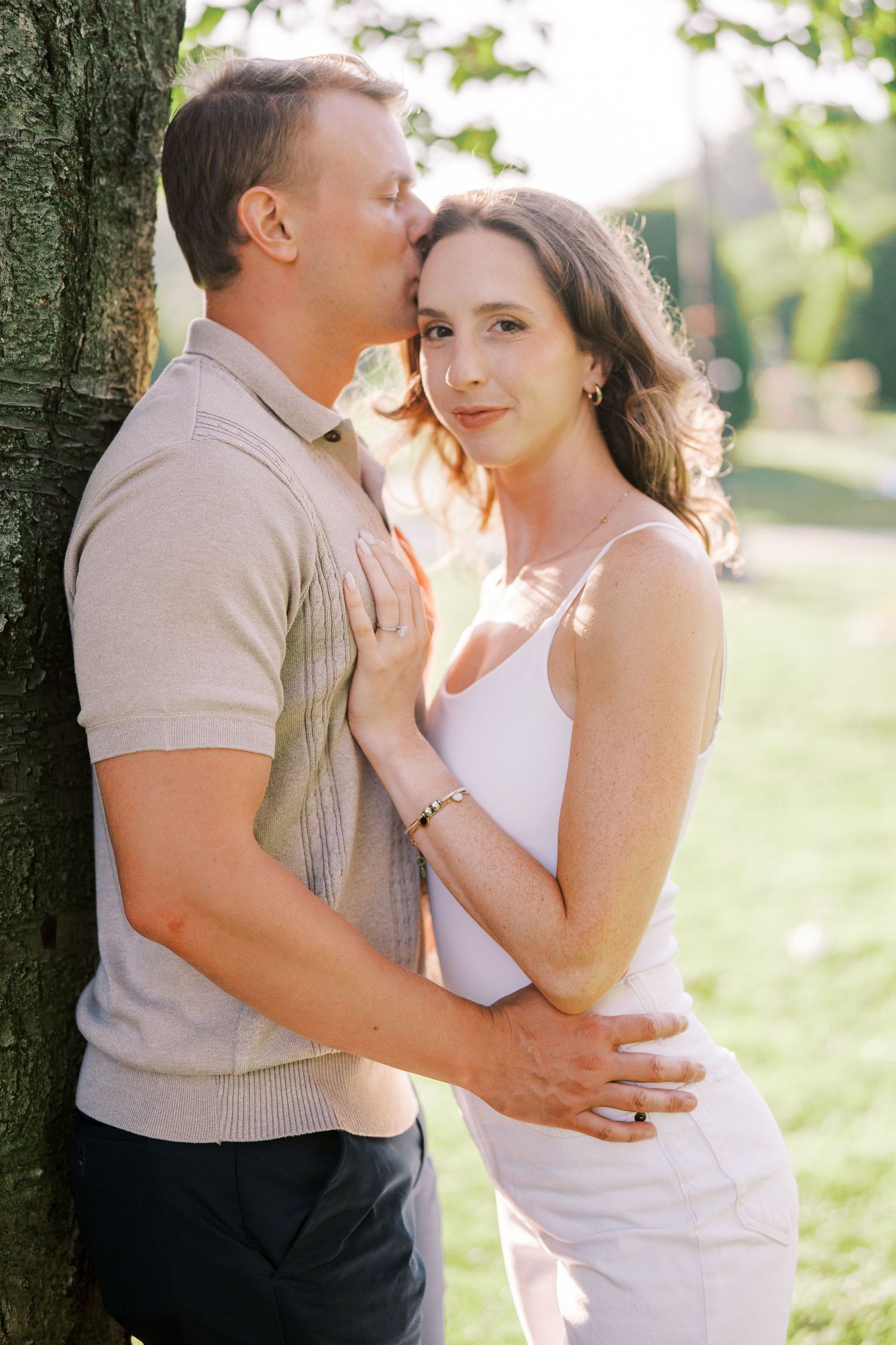 Intimate couple embraces outdoors in natural sunlight wearing white and beige clothing for romantic photoshoot.