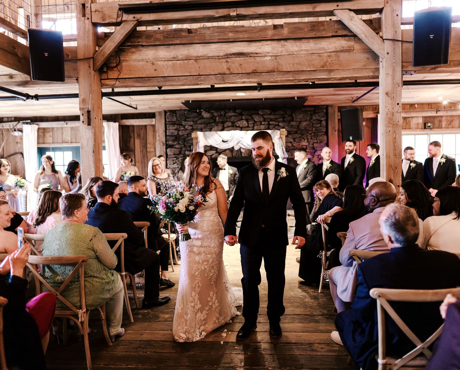 Wedding ceremony in rustic wooden barn venue with guests seated on both sides of aisle.