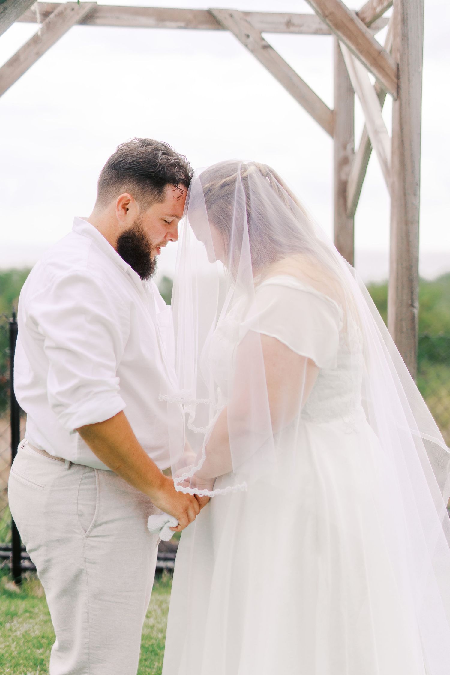 Sweet candid moments of a couple under a wooden pergola during their wedding ceremony.