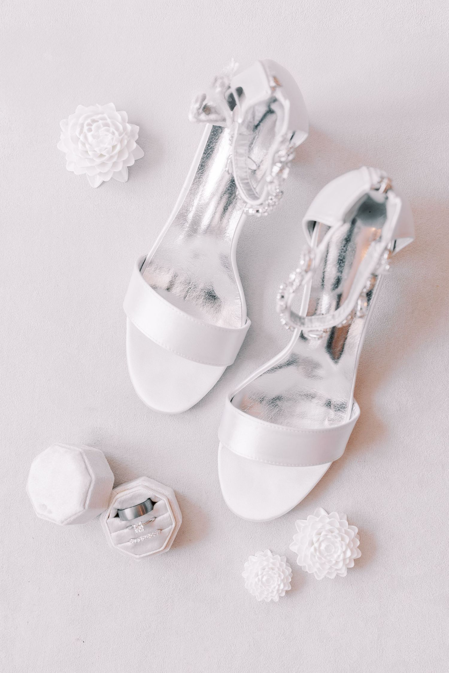 Elegant white bridal sandals with floral appliques arranged on a light background.