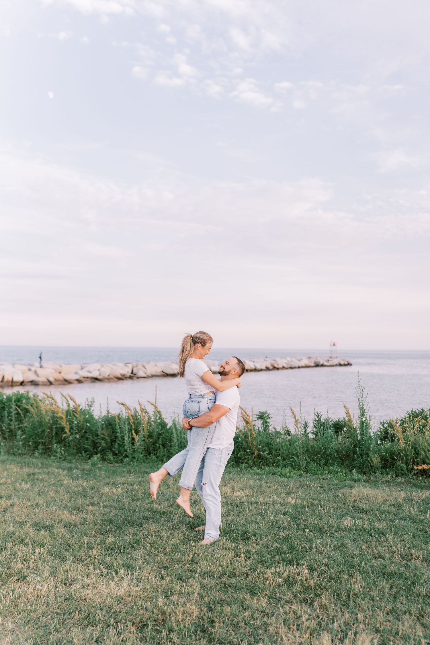 Joyful couple sharing playful lift moment by waterfront at sunset.