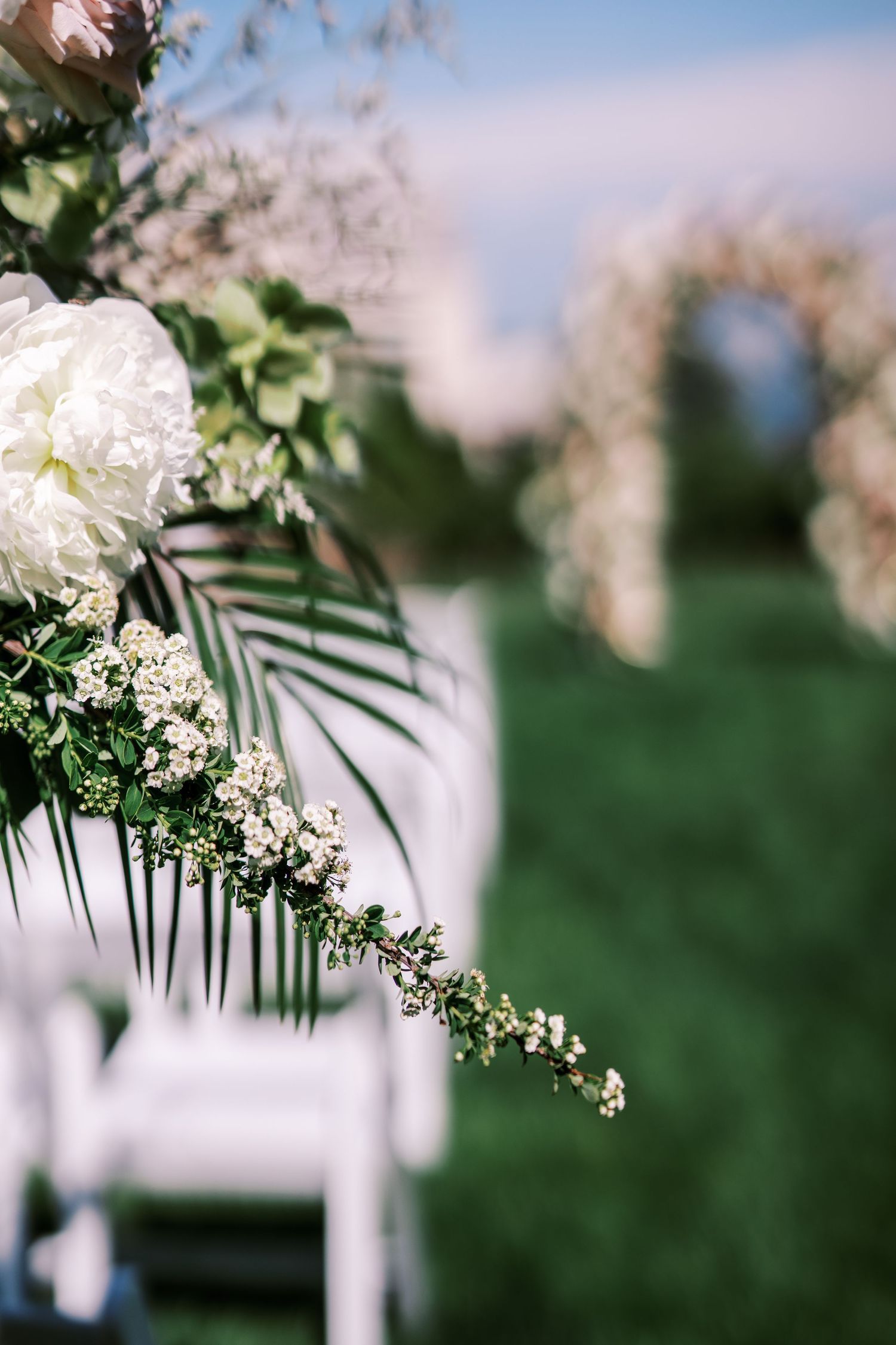 Delicate white floral arrangements with ferns and foliage create an elegant outdoor wedding ceremony backdrop.