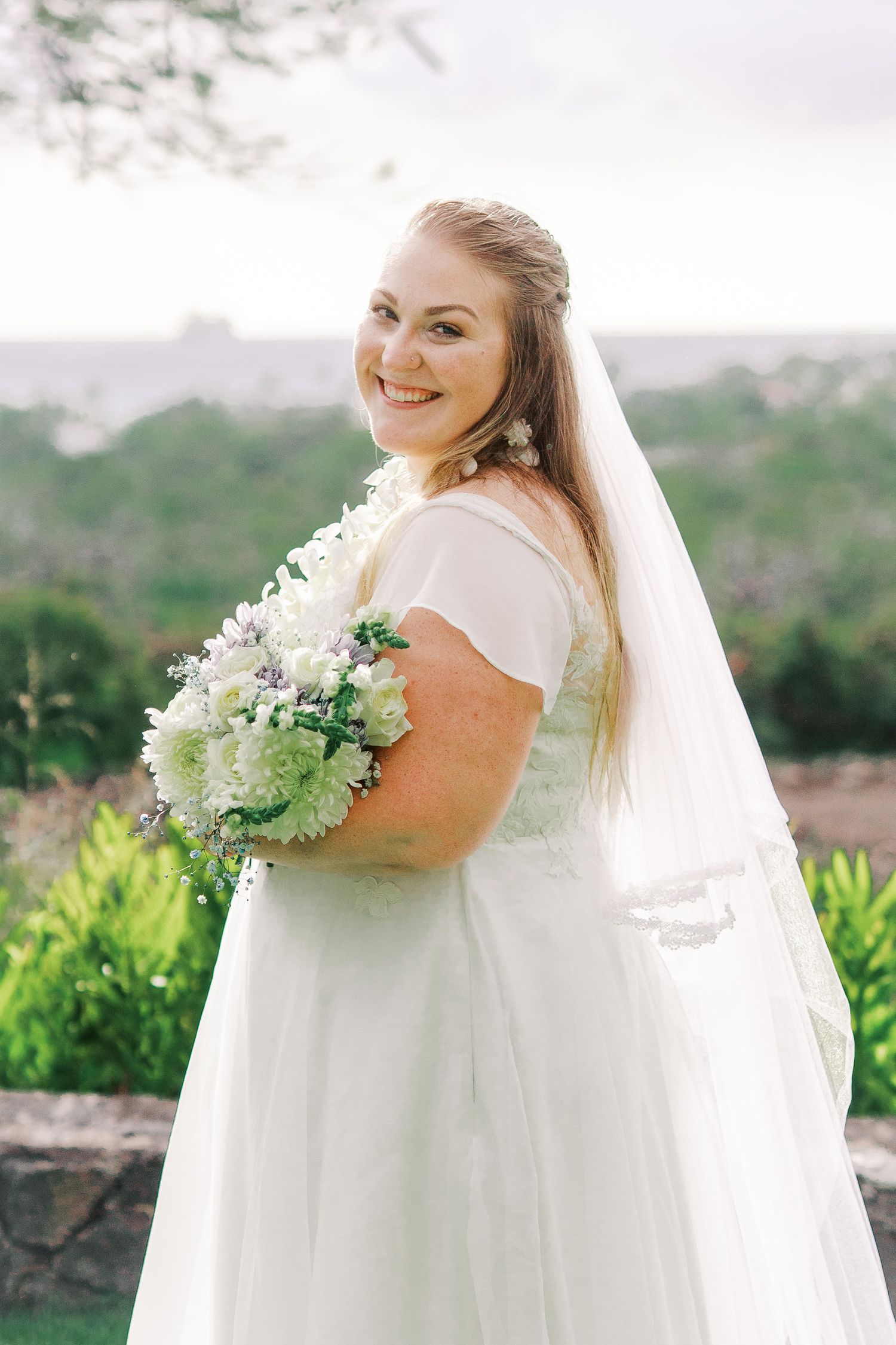Outdoor bridal portrait with bouquet against scenic mountain backdrop.