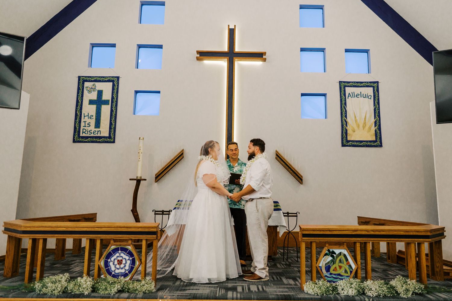 Light-filled chapel interior with modern stained glass windows and a wooden cross on the altar.
