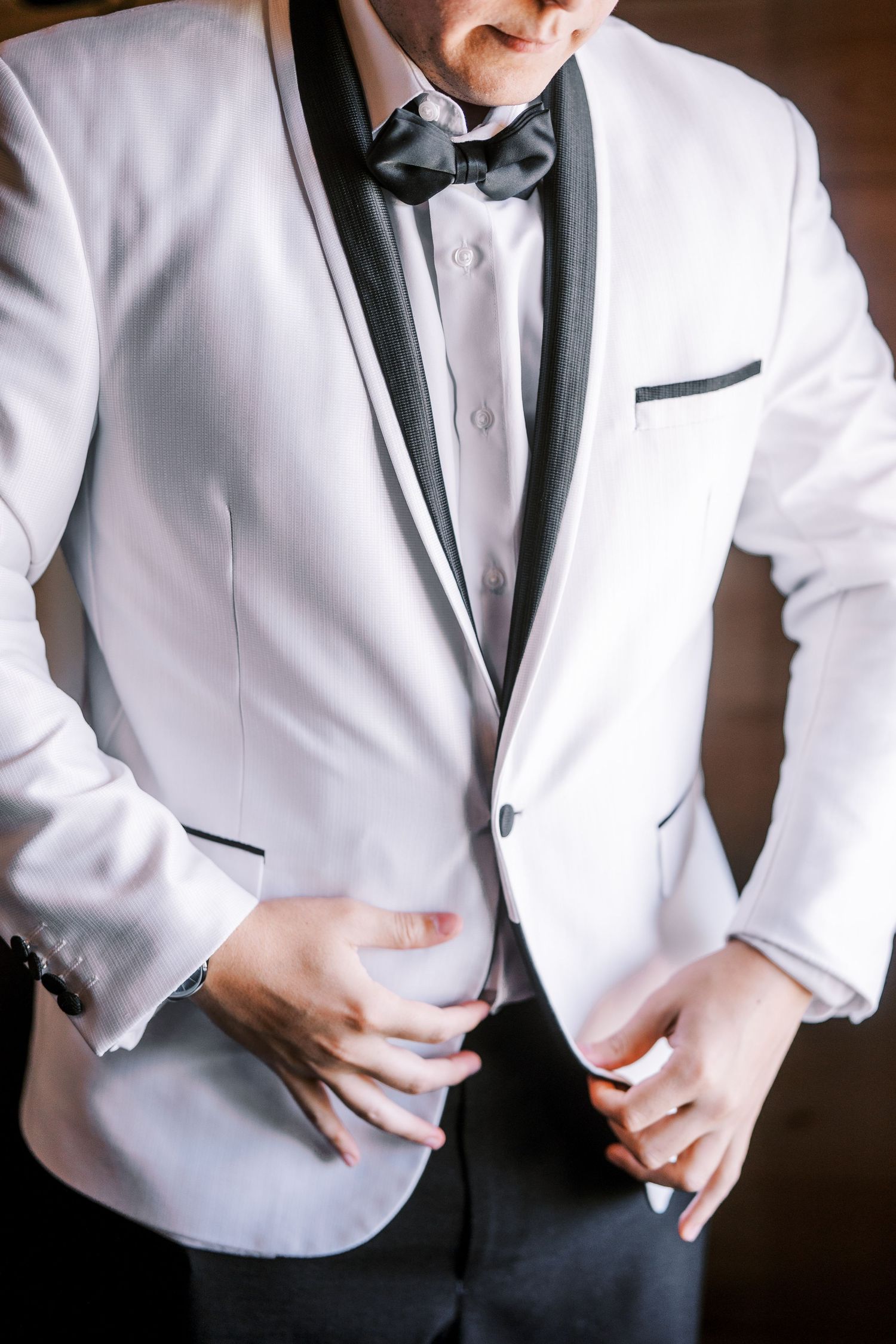Close-up view of white tuxedo jacket with black bow tie and lapels being adjusted by the wearer.