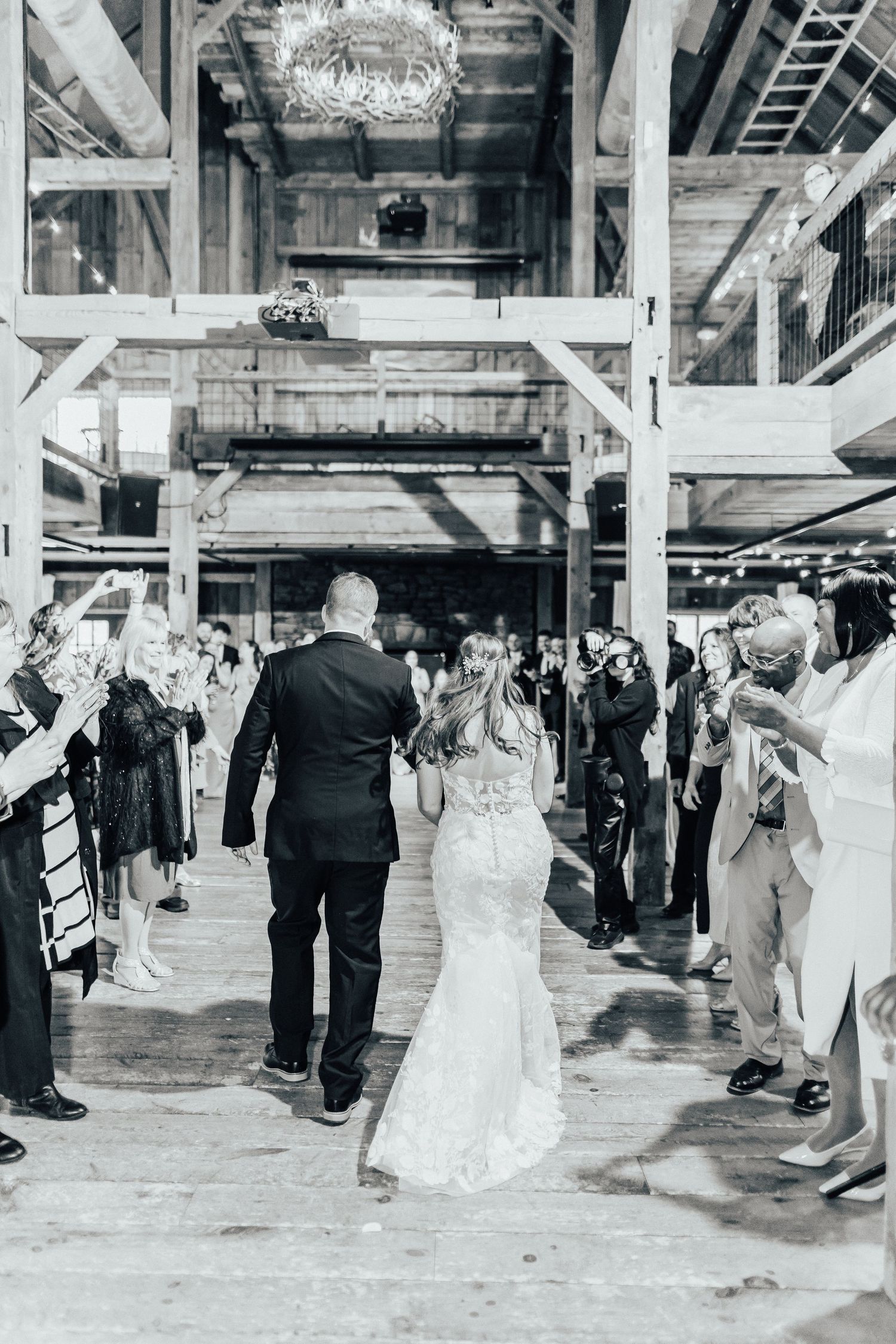 Wedding couple making grand entrance through barn venue walkway lined with guests.