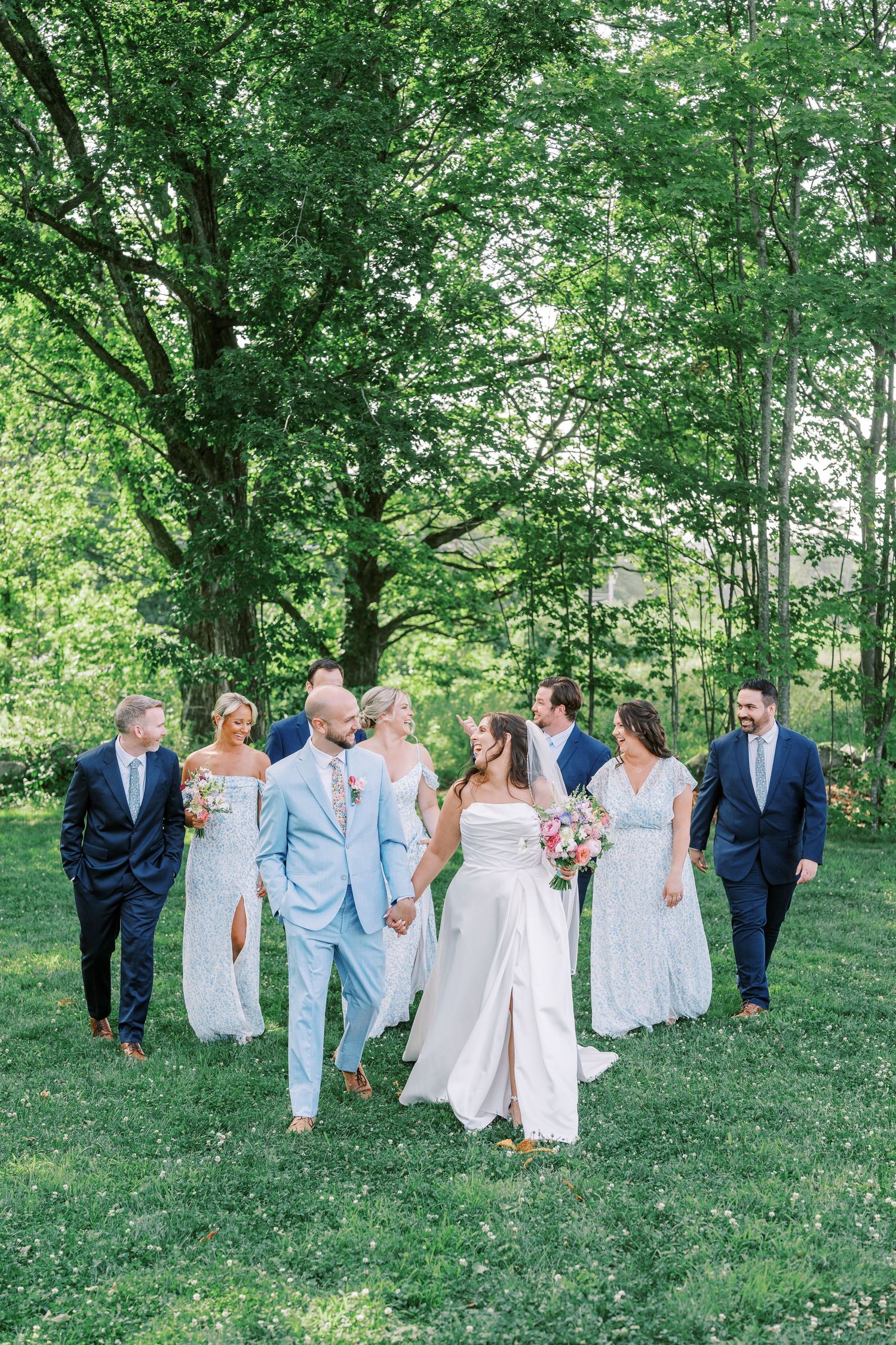 Wedding party walking together on a grassy hillside wearing blue and white attire.
