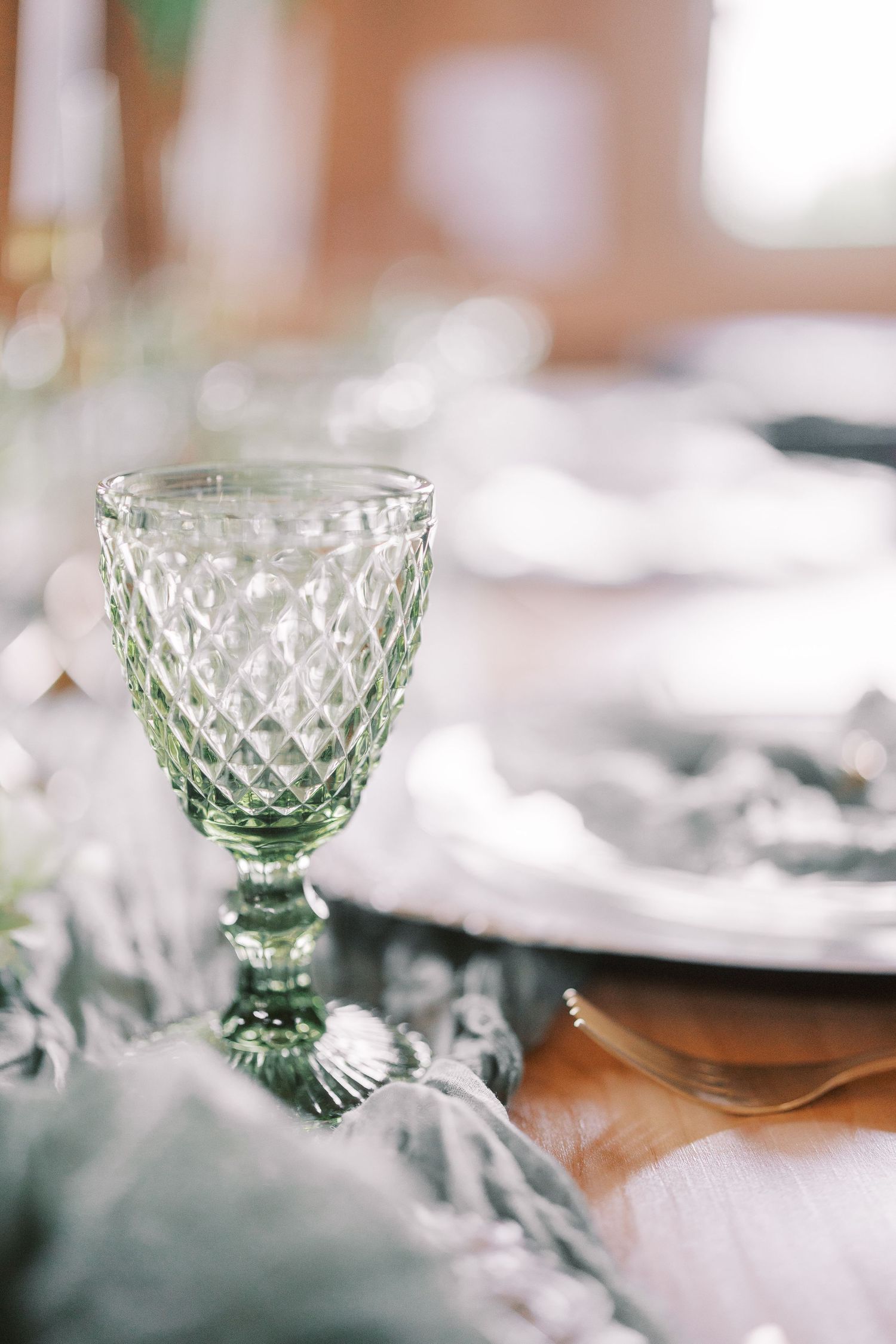 A vintage green glass goblet with diamond pattern sits elegantly on a light colored table setting.