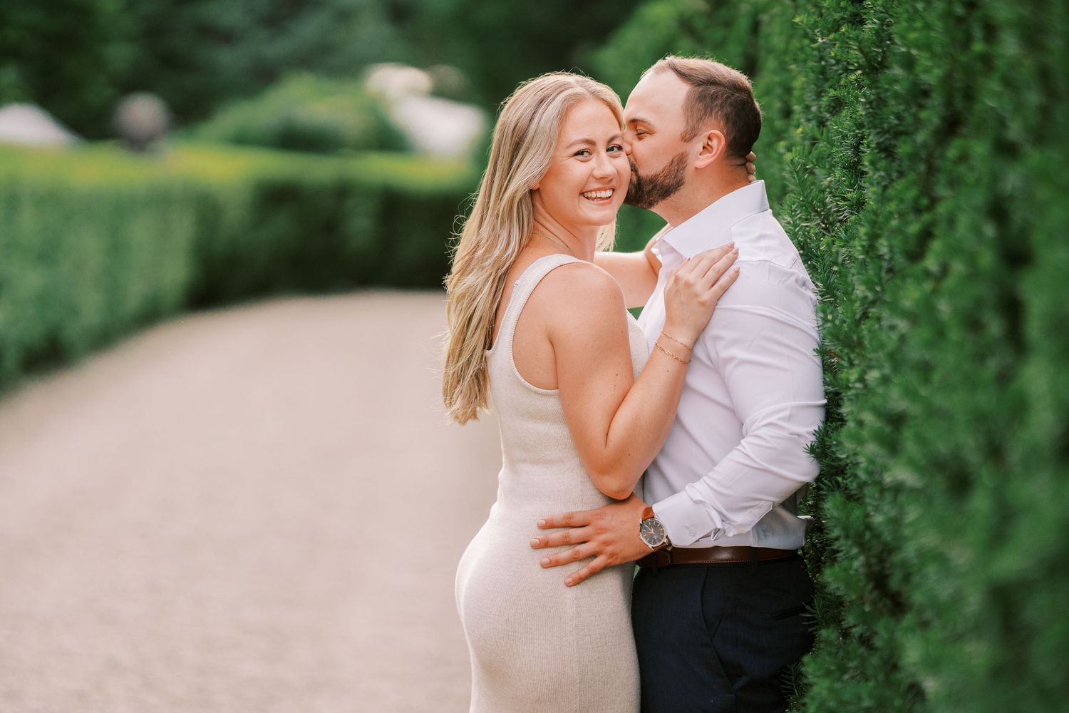 Intimate moment captured between a couple in white clothing against a garden backdrop.