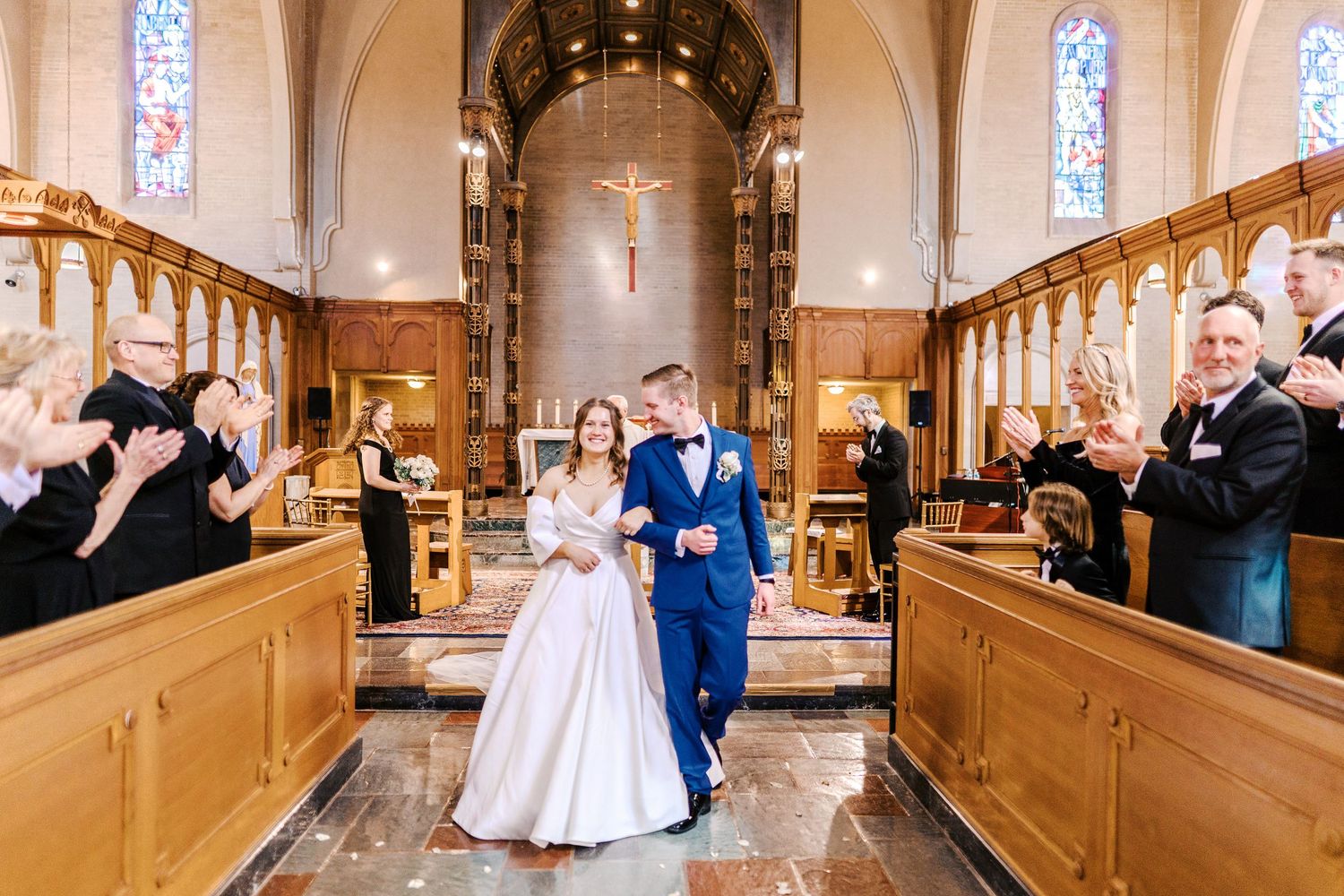 A couple walks down the aisle in a church sanctuary while guests in wooden pews celebrate their joyful union.