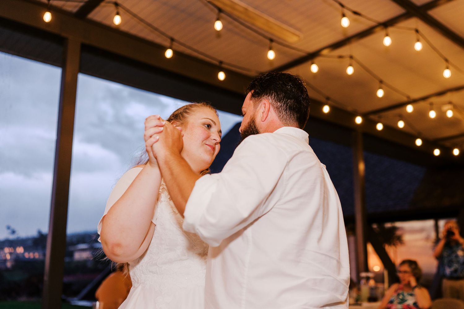 A couple shares their first dance under warm string lights at their wedding reception.