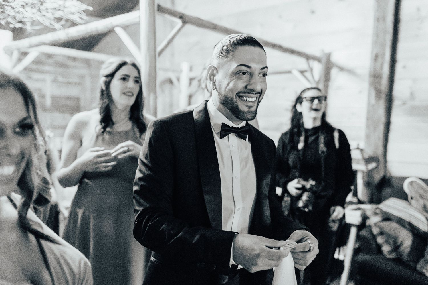 Black and white photo of guests laughing at an outdoor wedding reception with formal attire.