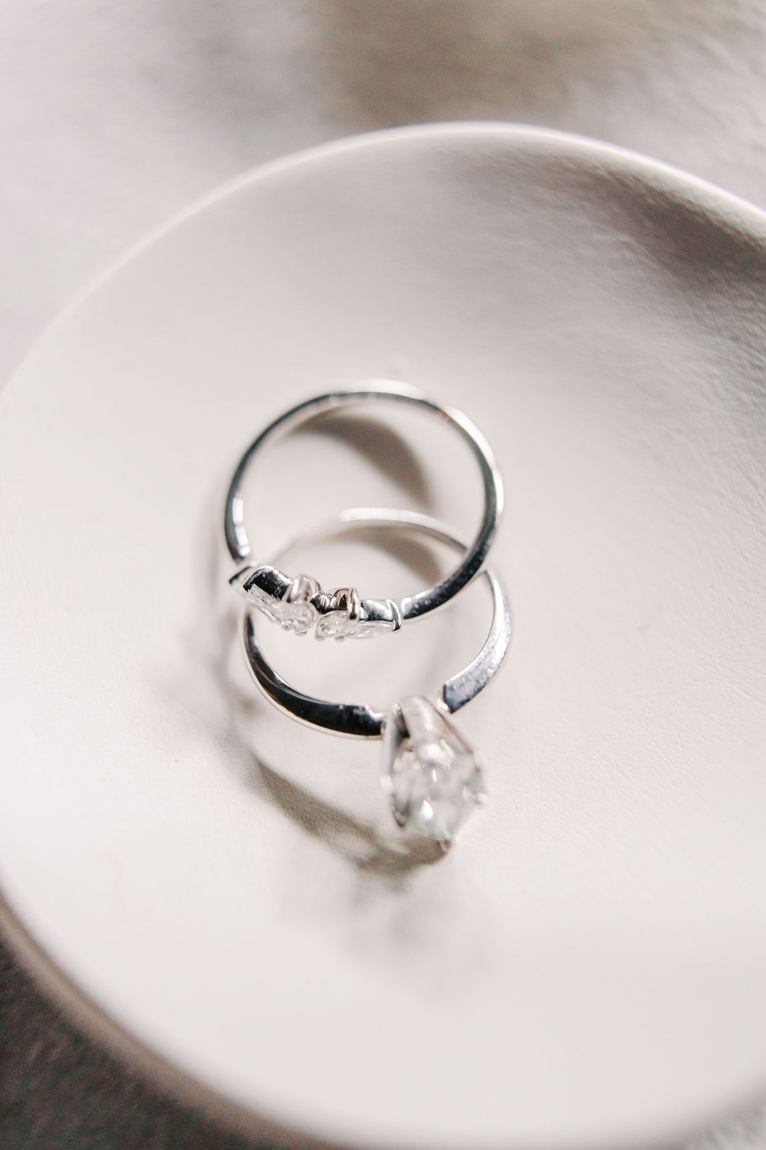 Diamond engagement ring and wedding band resting on white ceramic plate.