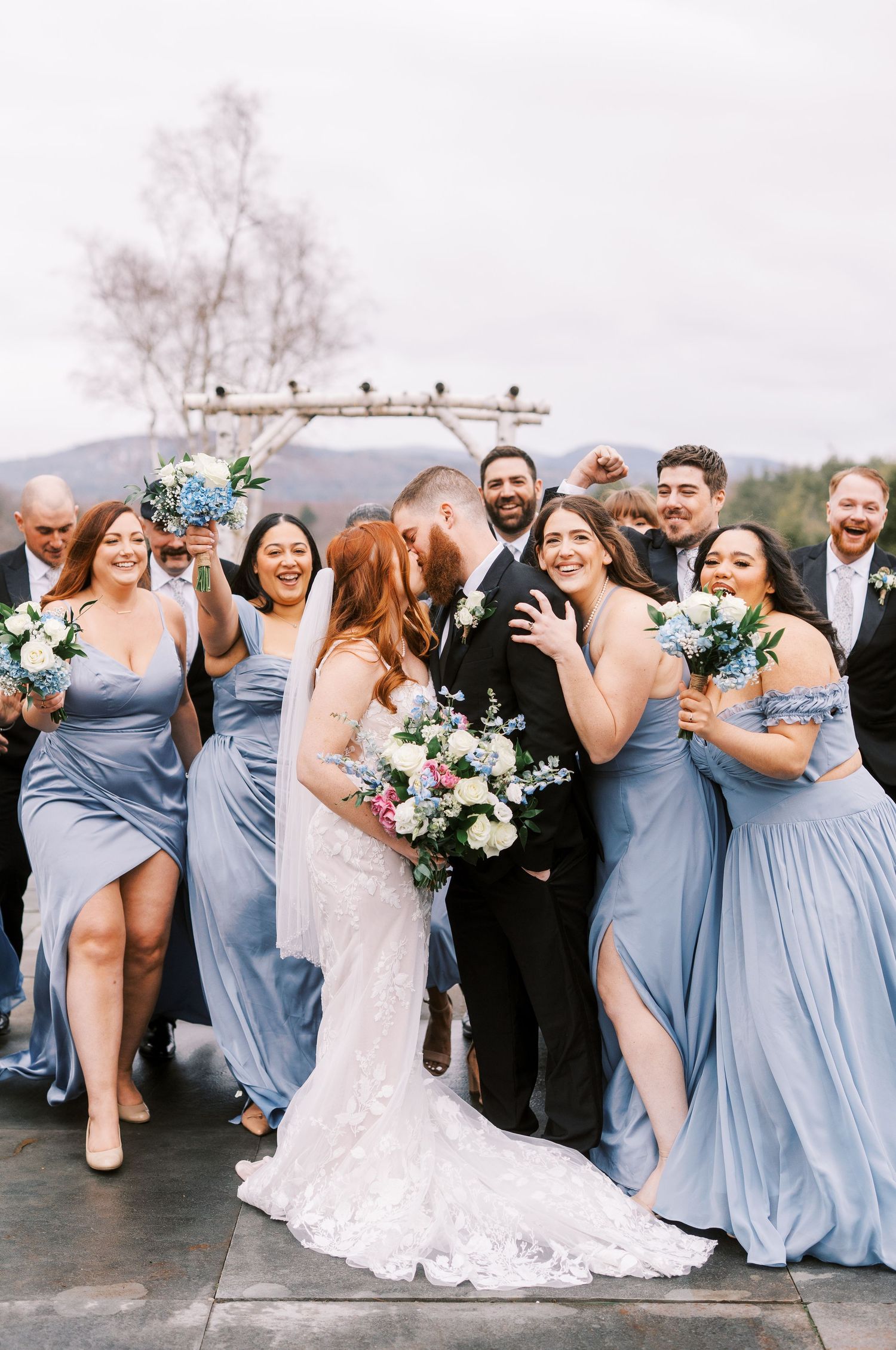 Wedding party in light blue bridesmaid dresses celebrating outdoors with bouquets.