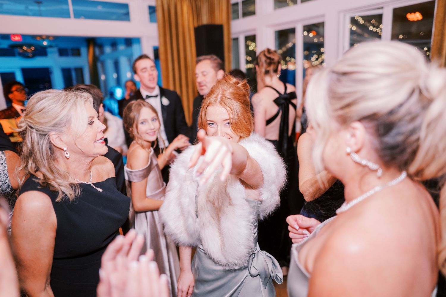A lively wedding reception dance floor scene with people laughing and dancing joyfully in an indoor venue.