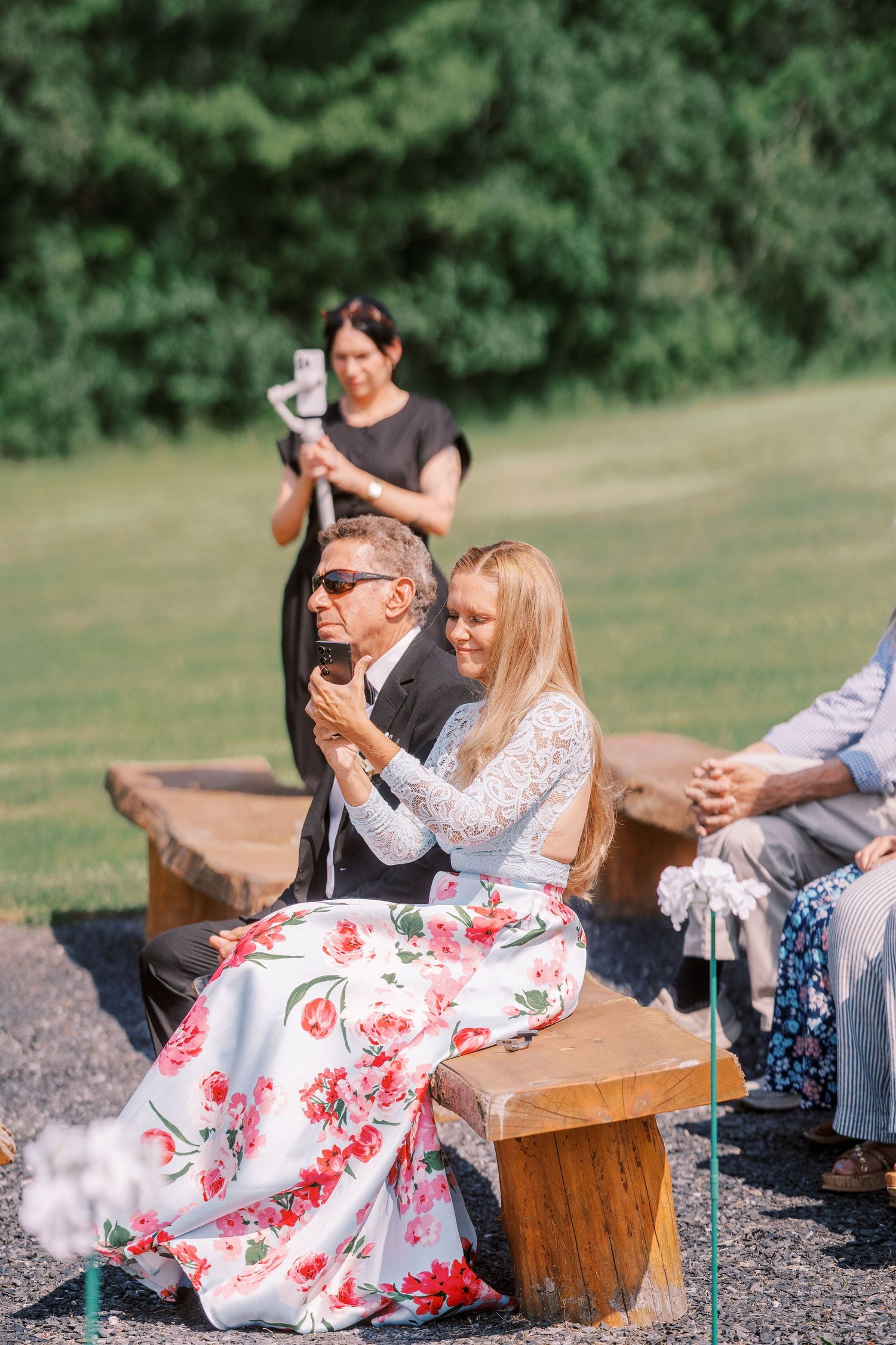 Couple sitting together at rustic wooden bench outdoors on lawn enjoying summer afternoon.