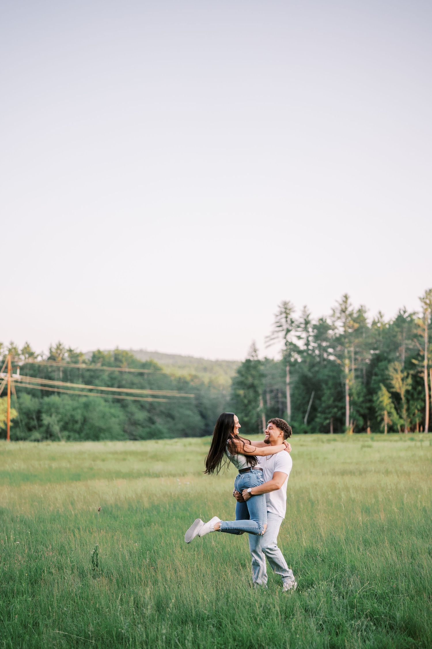 A couple sharing playful and romantic moments together in a sunny meadow with trees in the background.