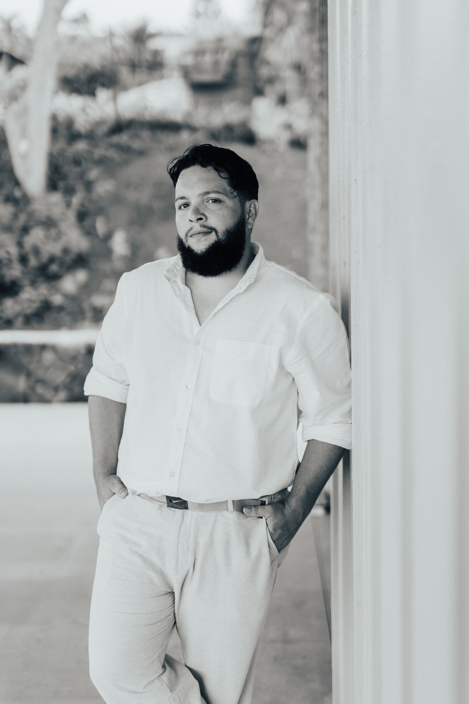 Person in white clothing leaning against a white pillar on a covered porch.