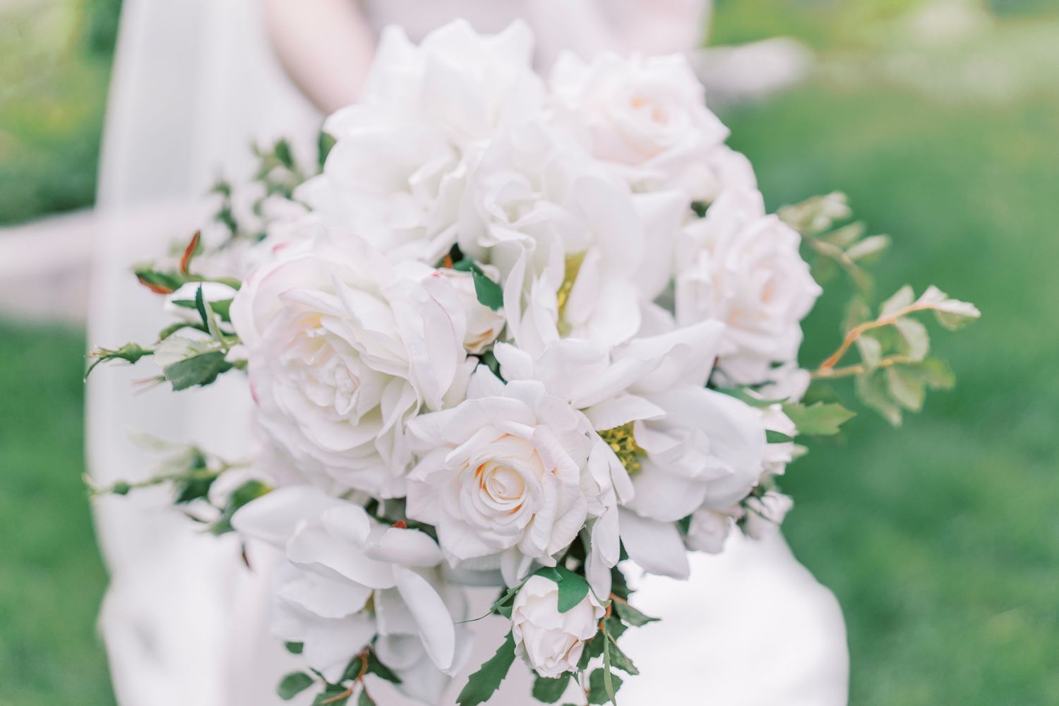 Elegant white rose and floral wedding bouquet with greenery accents against a soft blurred garden background.