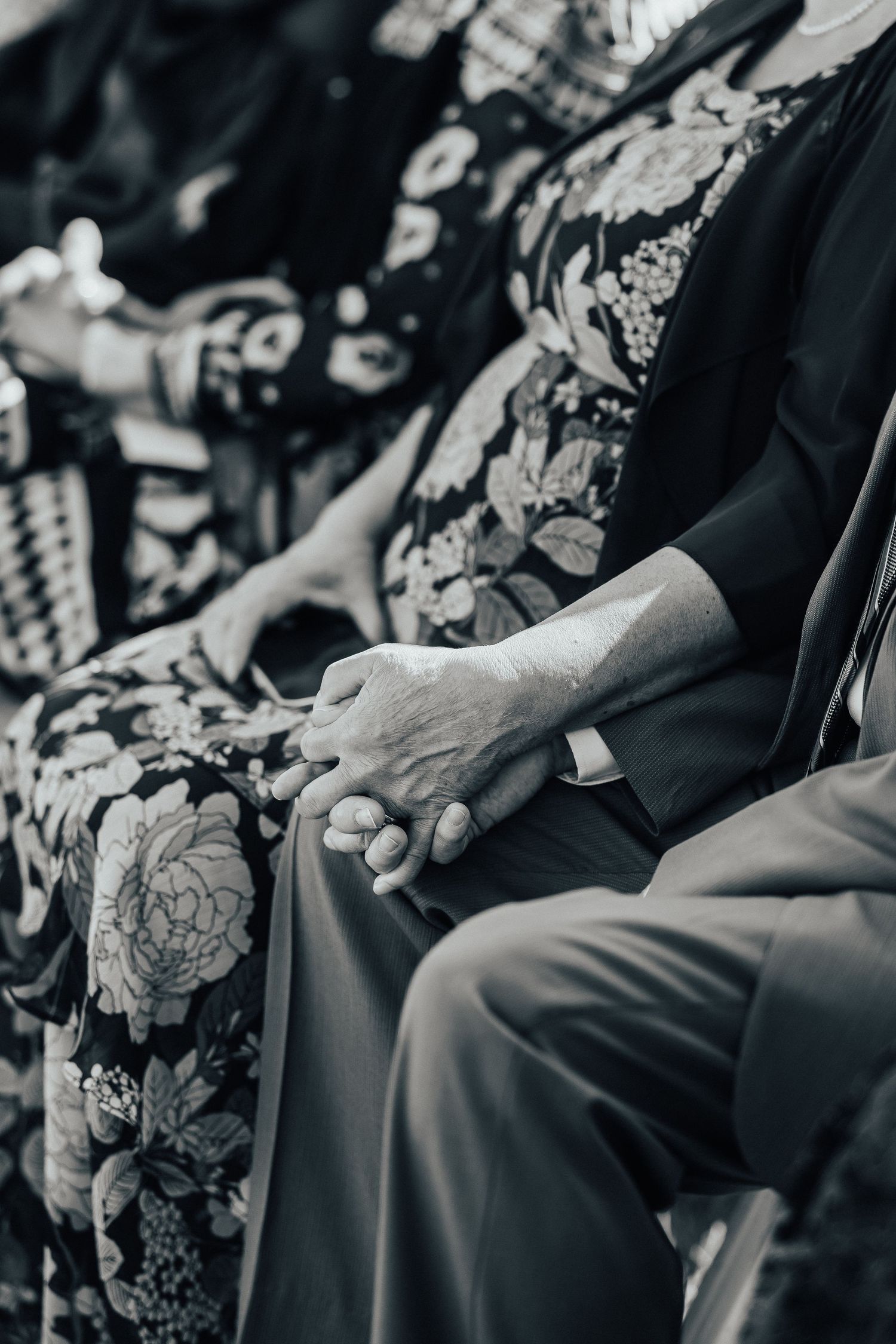 Elderly hands in monochrome resting on dress clothes, showing rings and textured skin details in a candid moment.