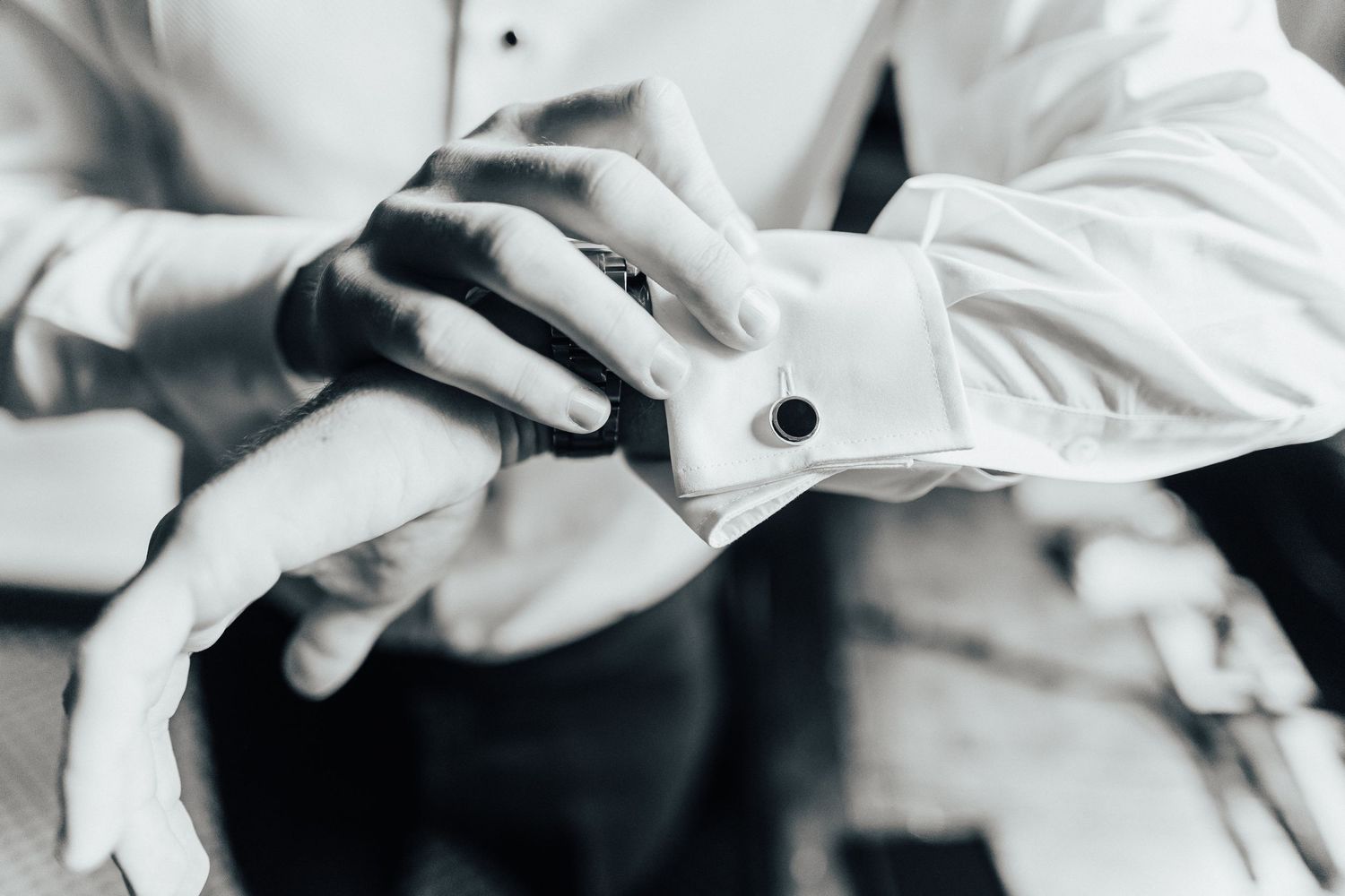 Close-up of hands in white sleeves buttoning up a formal dress shirt.