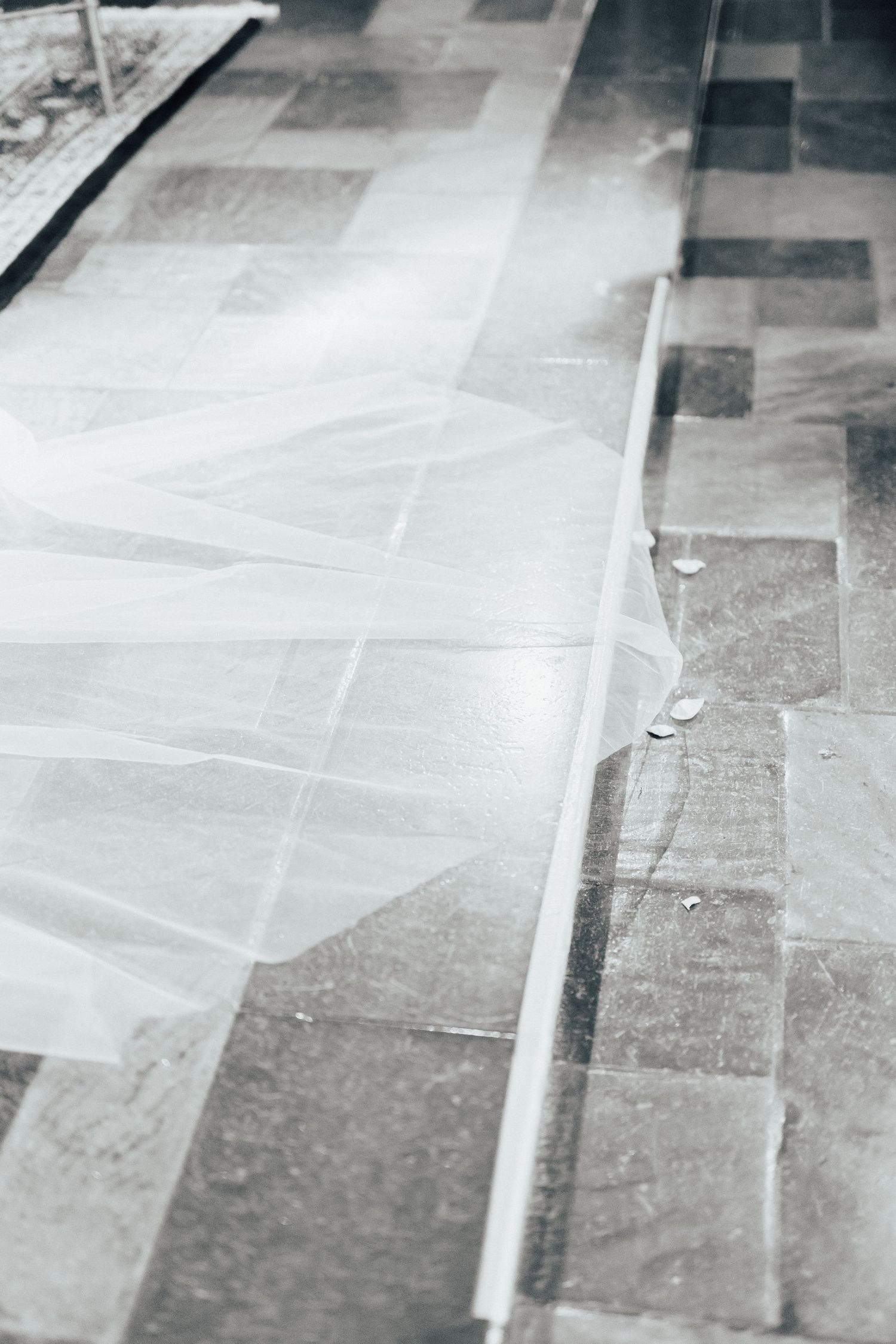 A close-up detail shot of a wedding dress train flowing across stone church floor tiles.