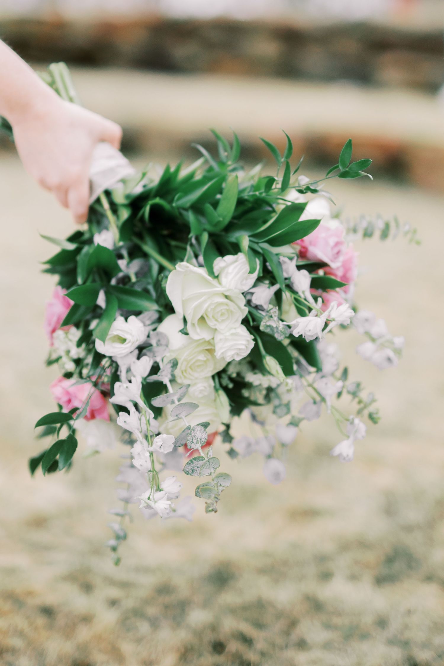 Elegant wedding bouquet featuring white roses, pink flowers and cascading greenery against natural backdrop.