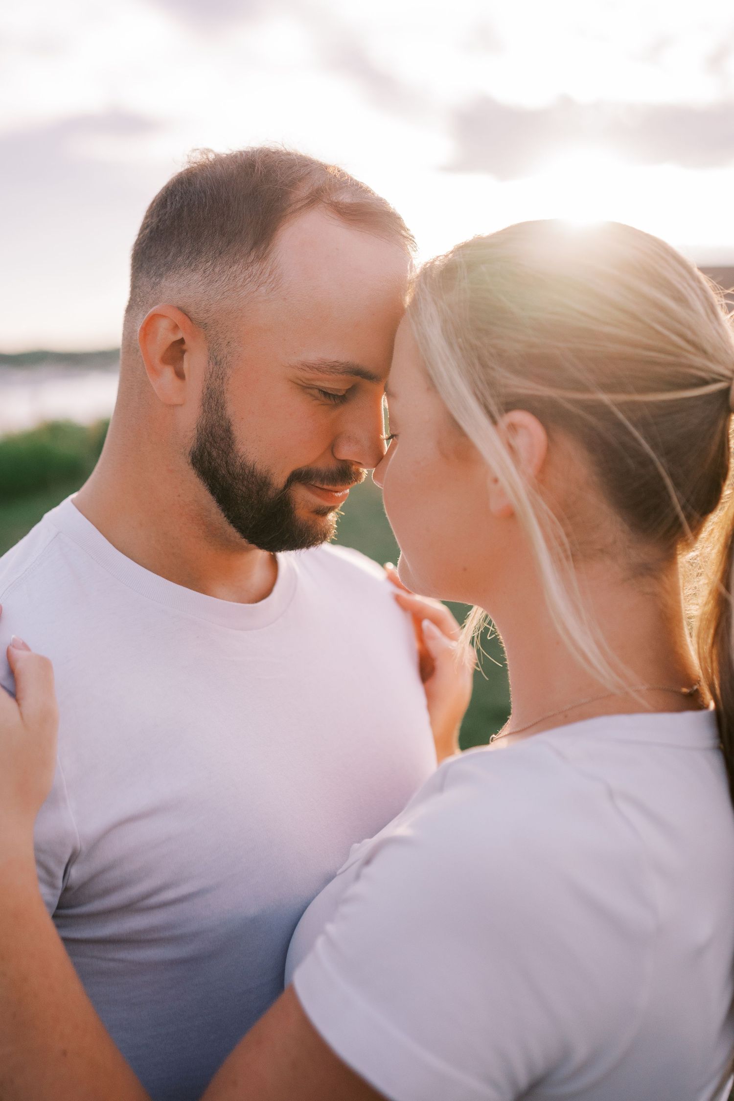 Romantic outdoor photoshoot with couple in white shirts against soft sunset lighting.