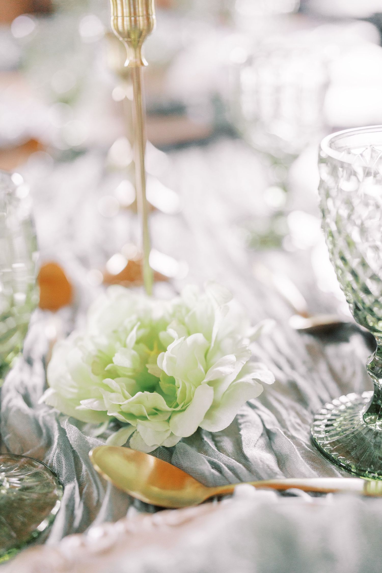 Elegant table setting with soft white flower centerpiece, gold cutlery and textured crystal glassware in dreamy light.