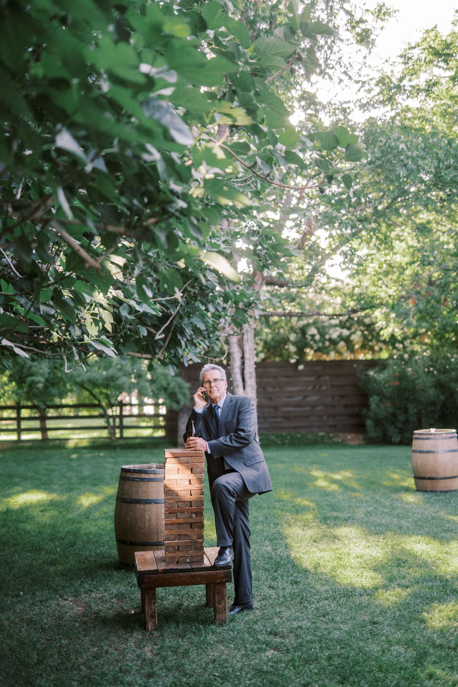A couple shares an intimate moment together on a rustic wooden bench near wine barrels in a lush garden setting.