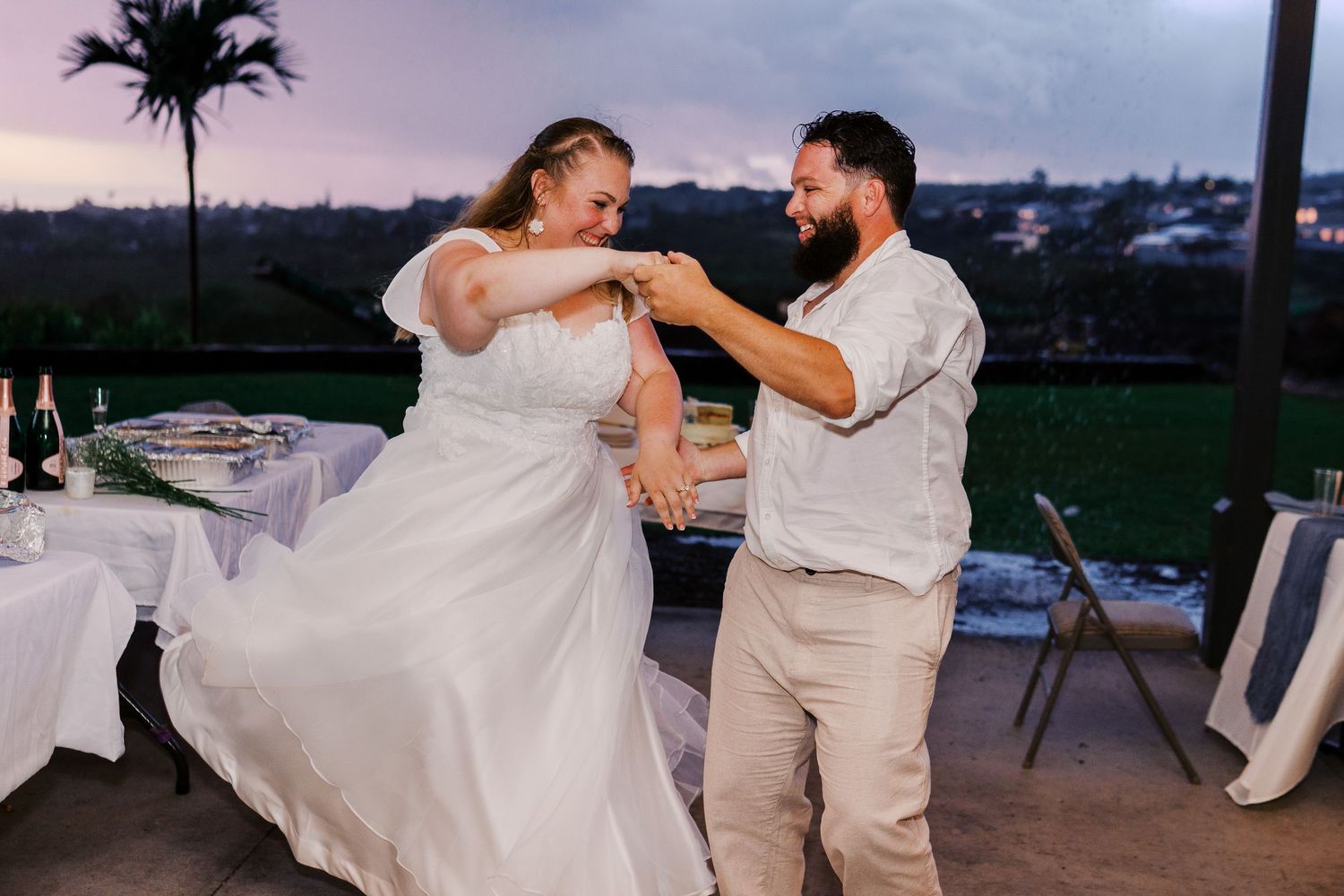 A newlywed couple dances together at their outdoor reception during sunset.